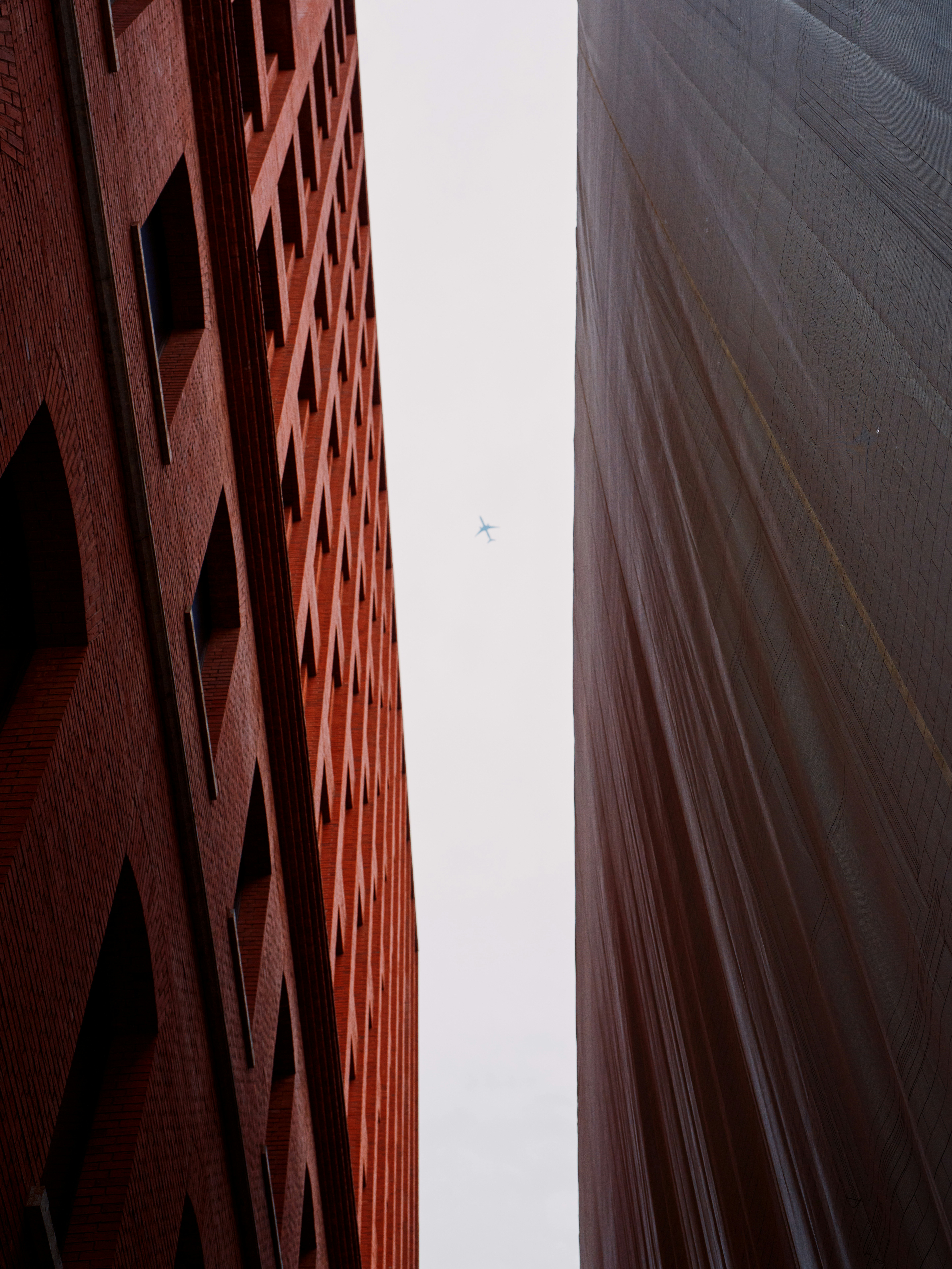 Gebäude umrahmen den Himmel, durch den ein Flugzeug fliegt.