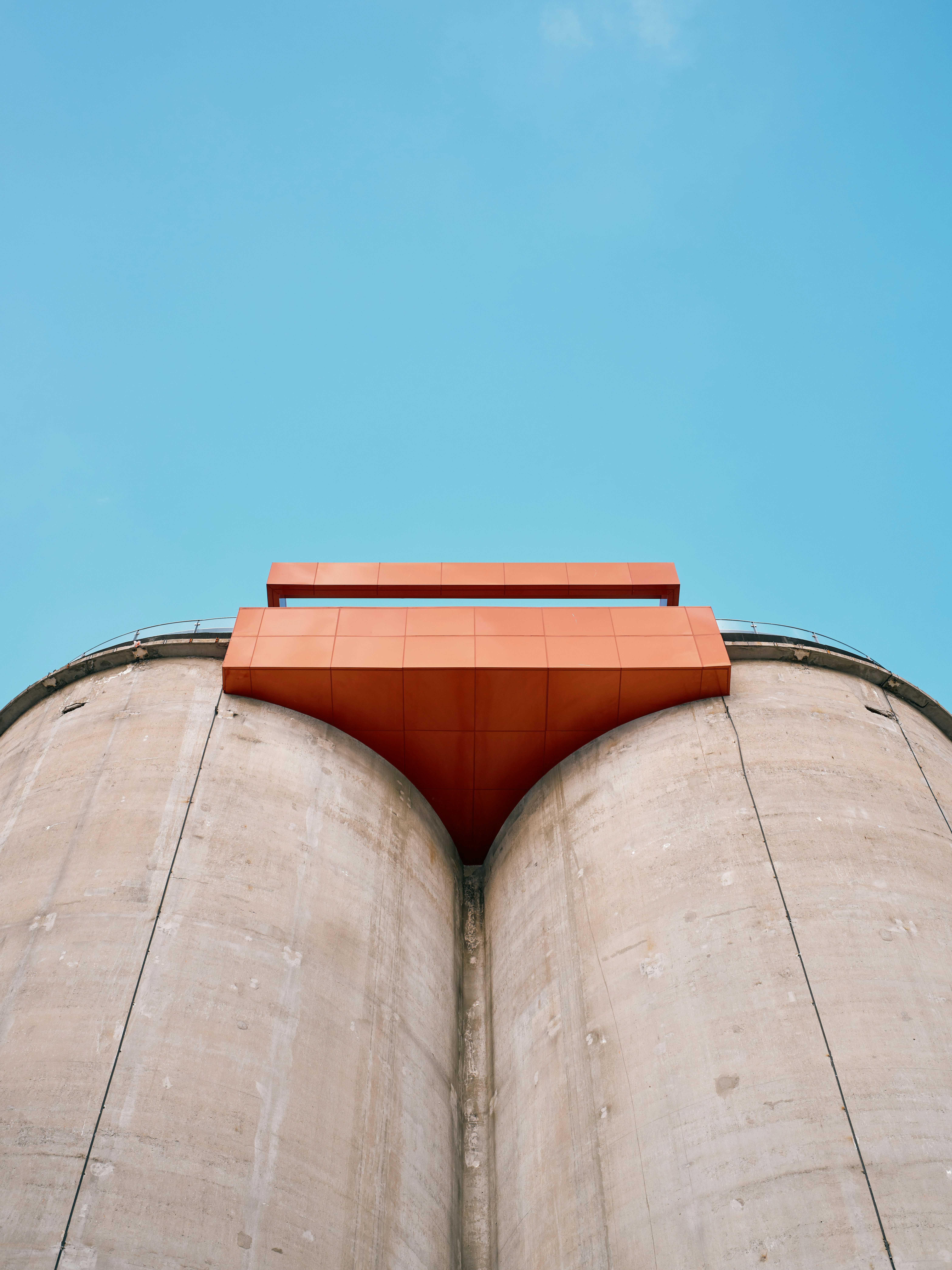 Silos mit orangefarbener Struktur vor blauem Himmel.