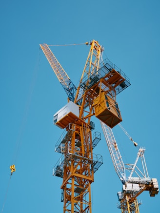 Construction cranes reach into a clear, blue sky.