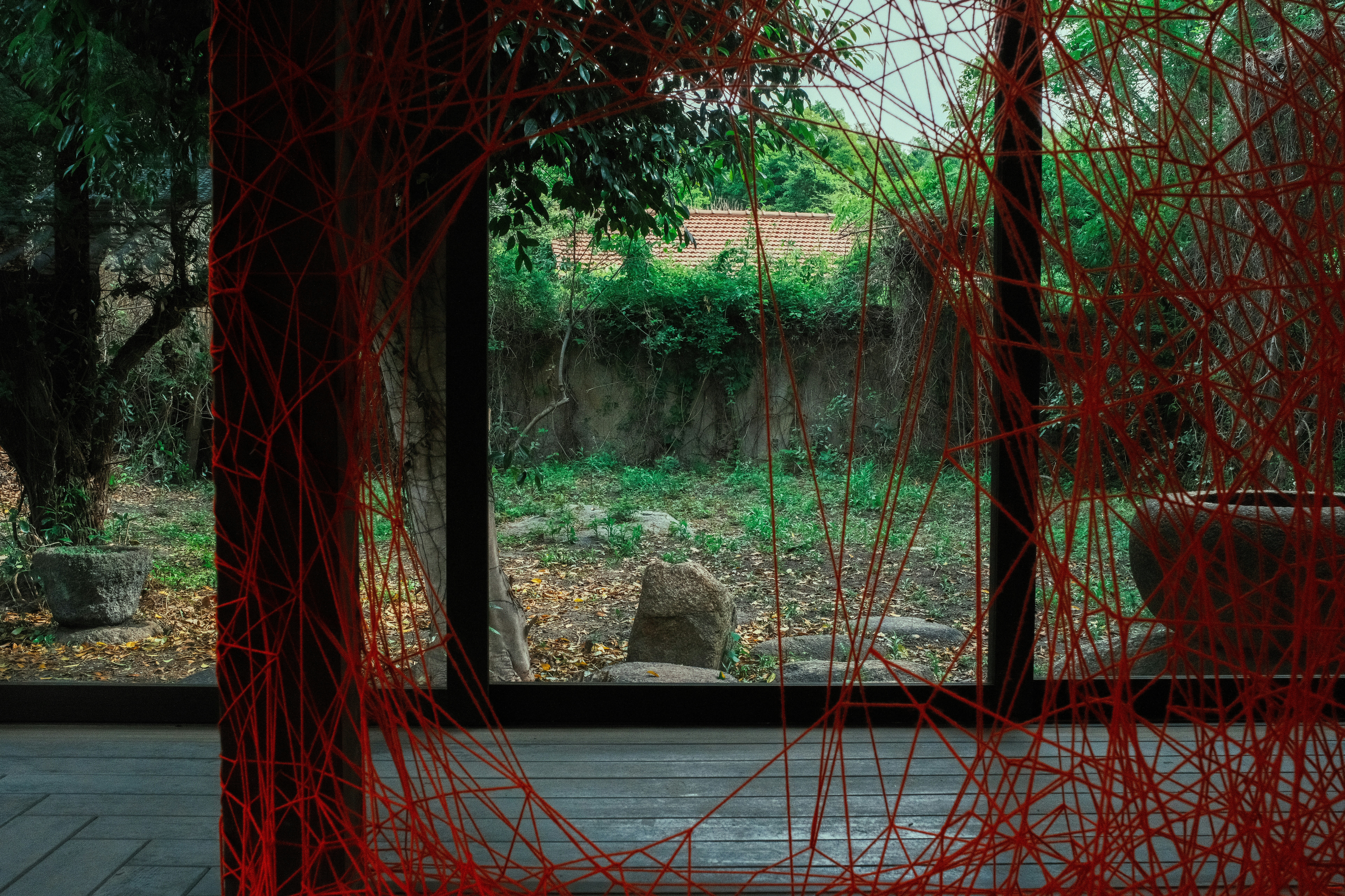 Red strings frame a window view of nature.
