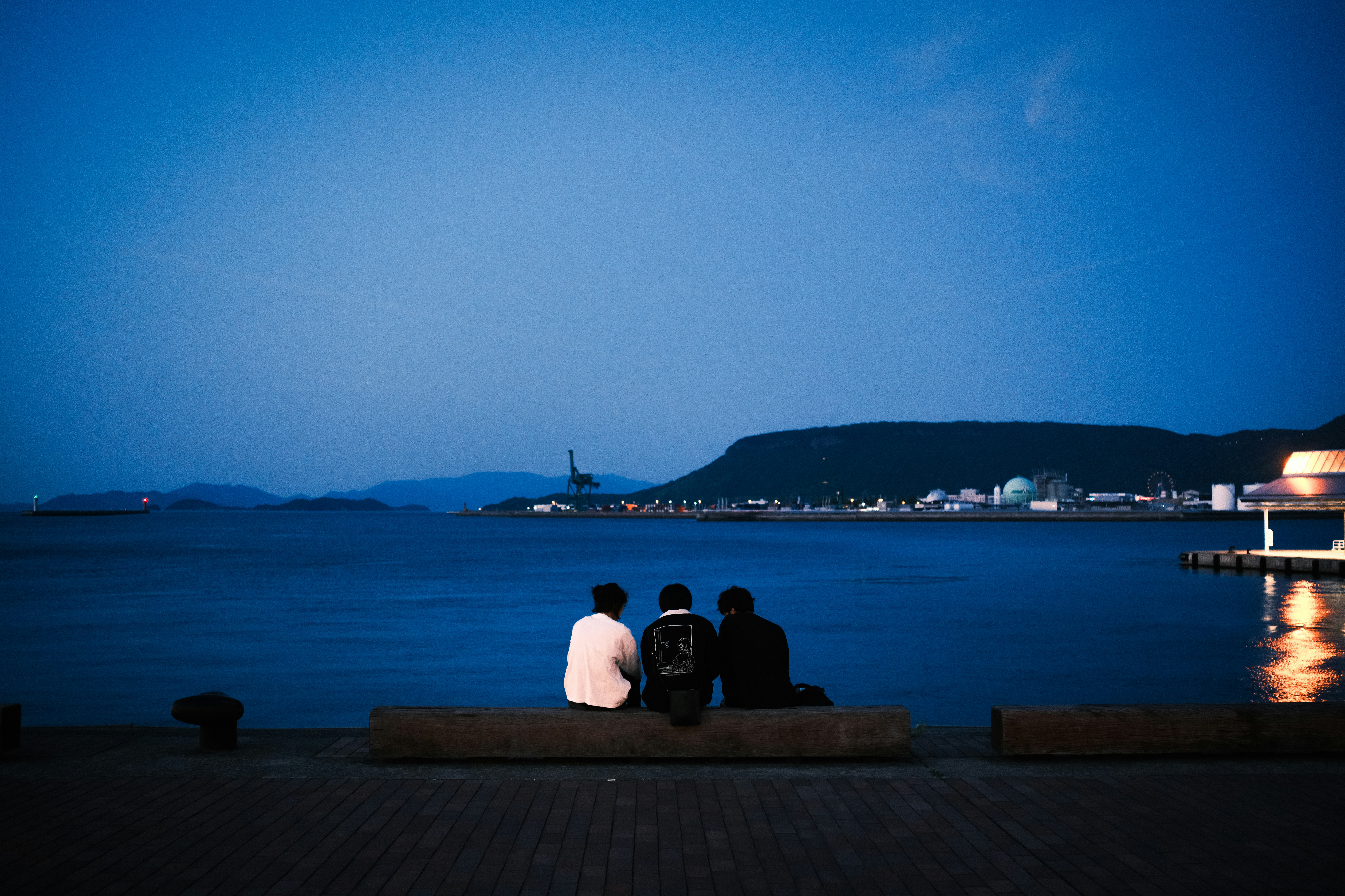 Three people sit and watch the dark water.