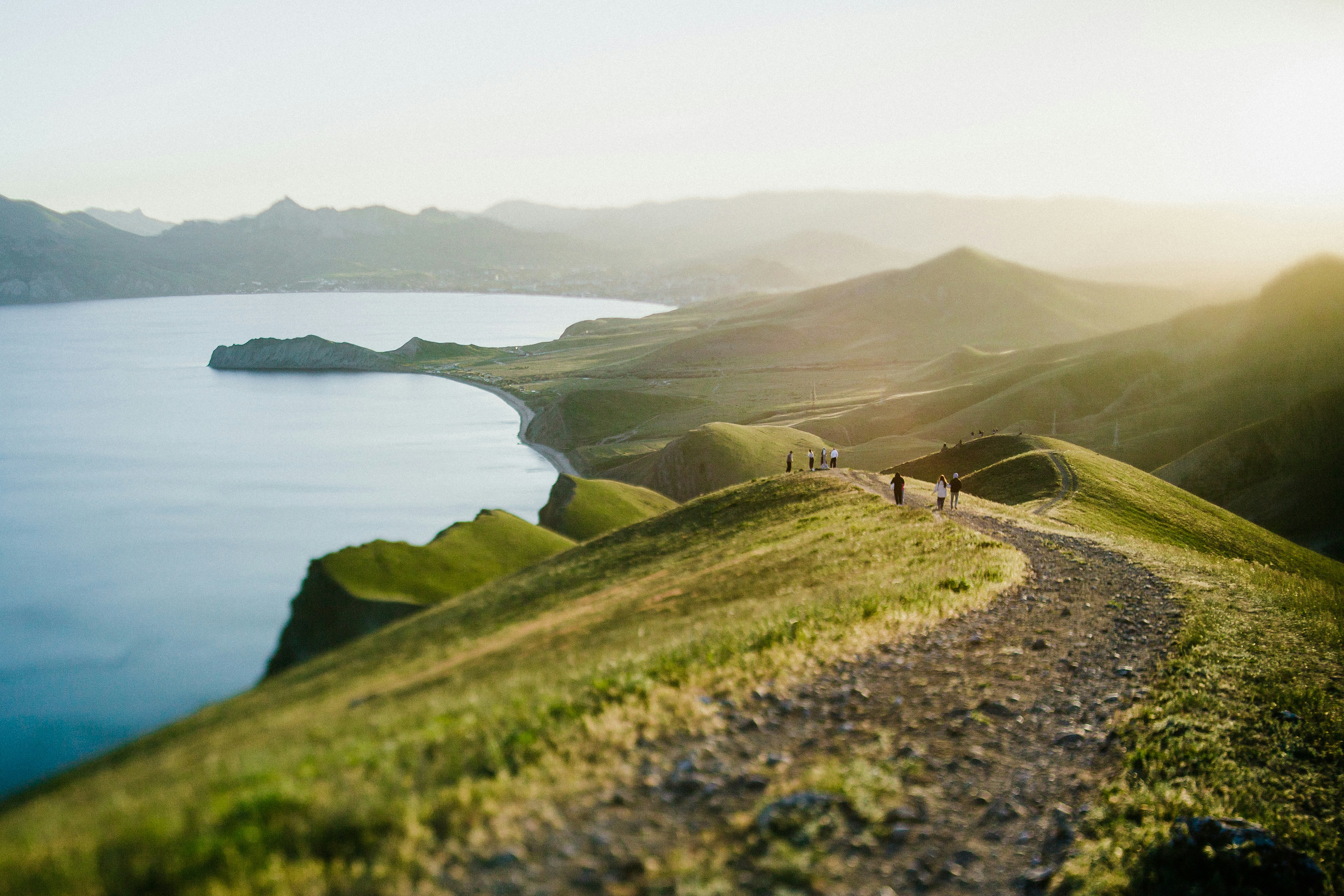 A path winds along a green ridge by the sea.
