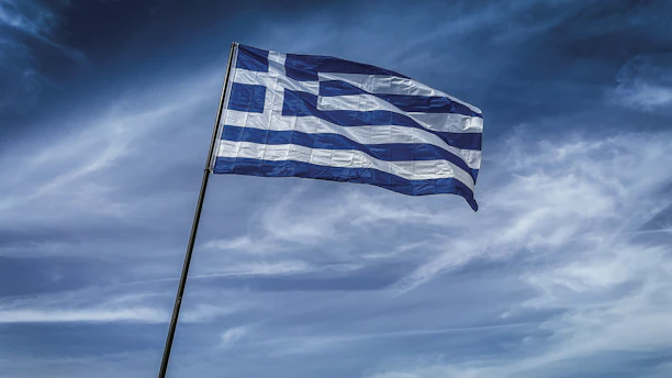 The greek flag flies against a cloudy sky.