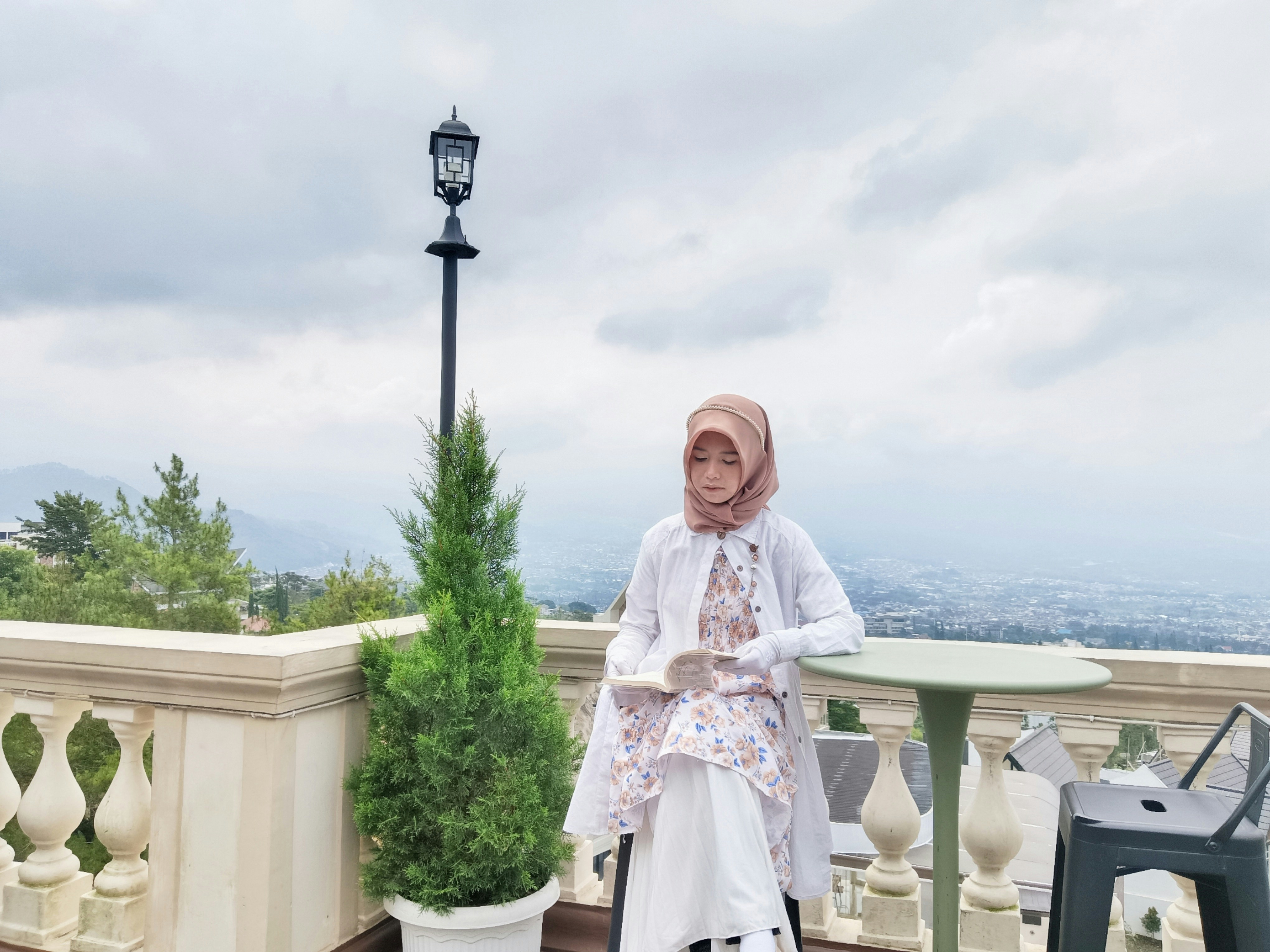 Wanita berpose di balkon dengan pemandangan indah.