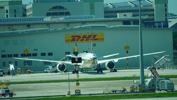 An airplane is parked in front of a dhl building.