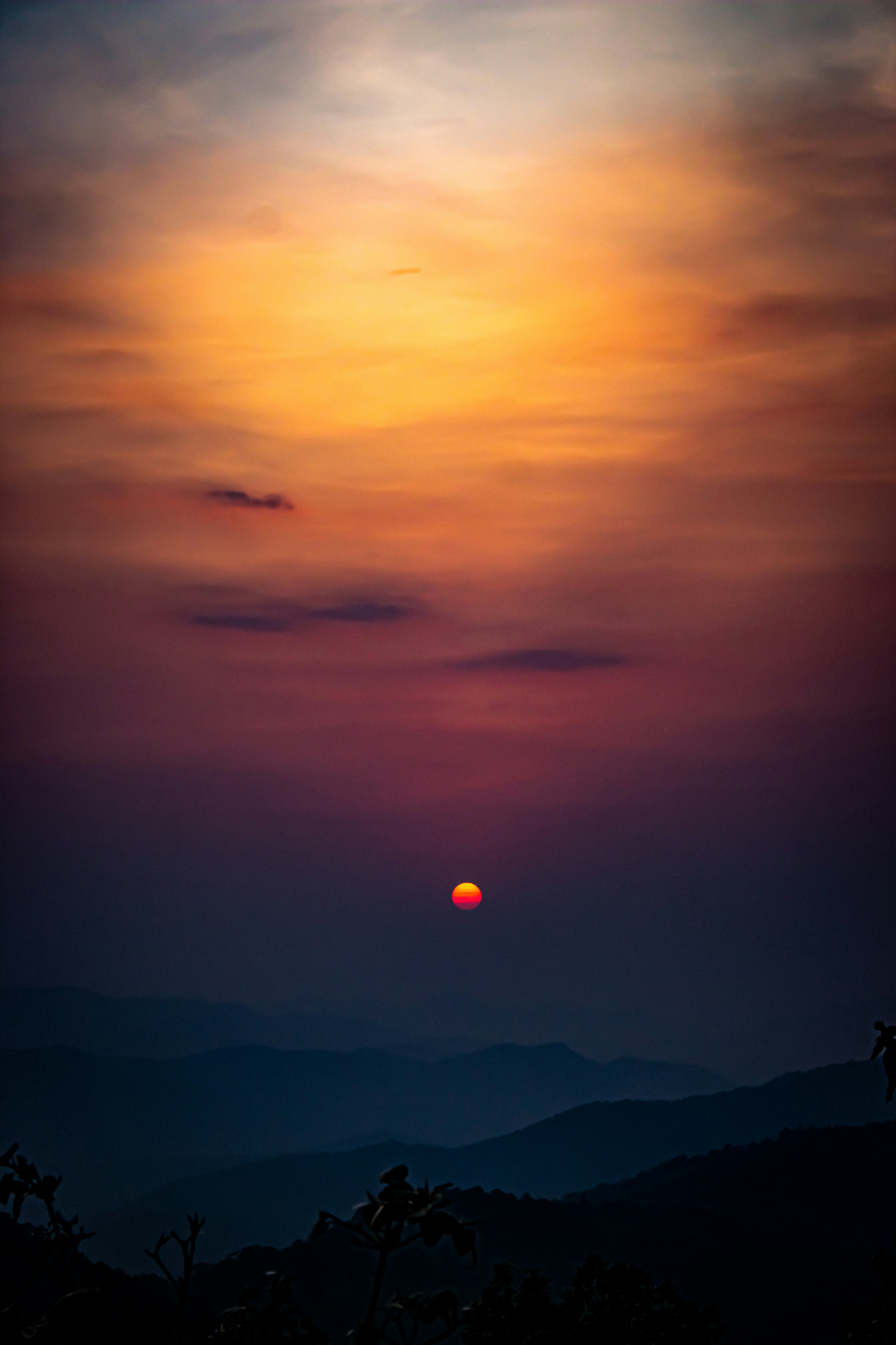 The sun sets over hazy mountains.