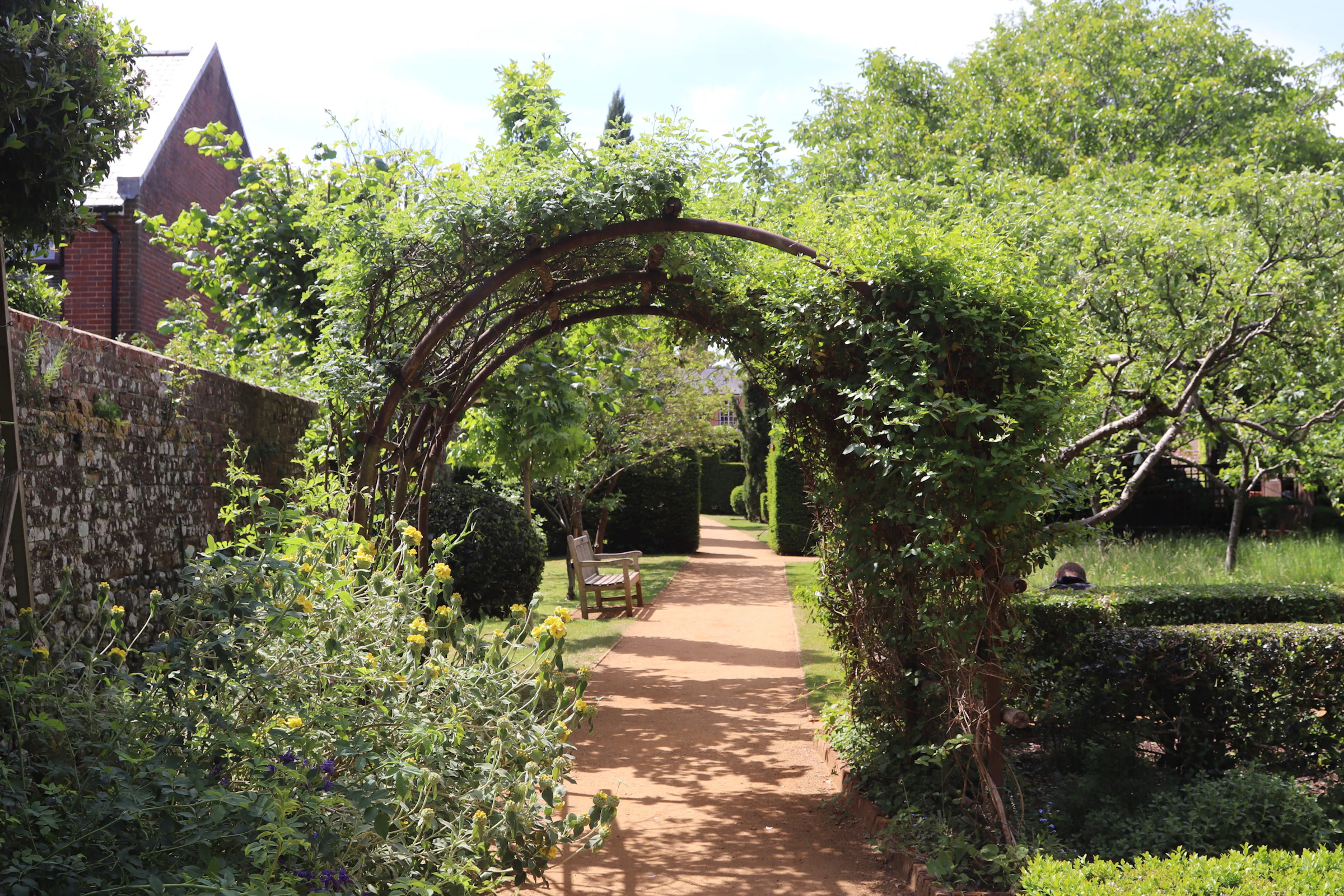A lush green garden path leading through a series of stone arches, framed by dense foliage