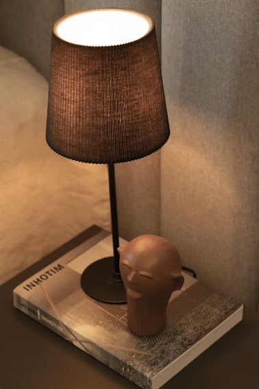 A lit lamp sits atop a bedside table.