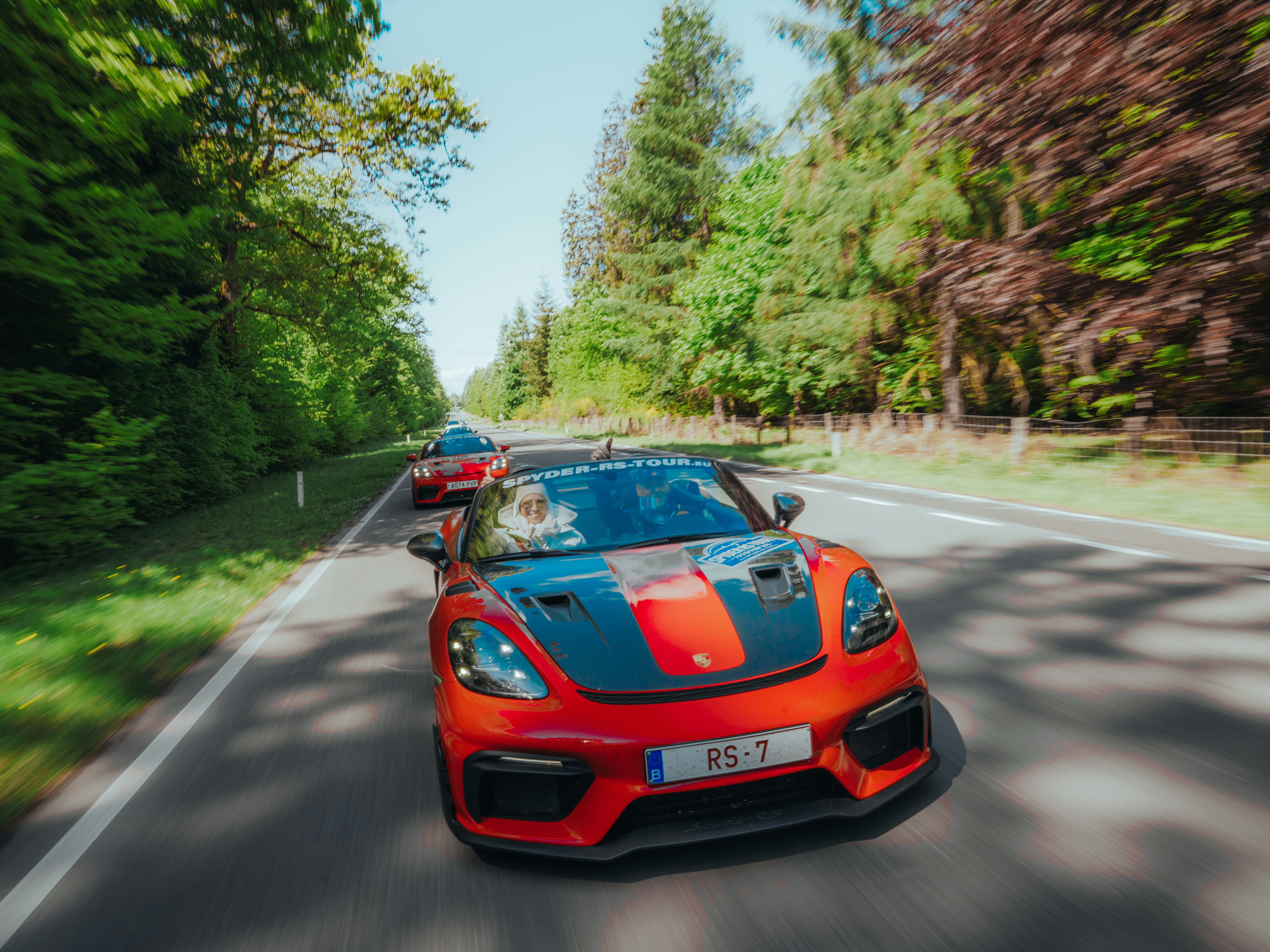 Sporty cars speed along a scenic forest road.