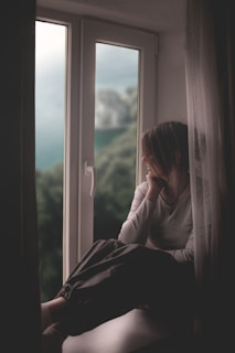 A woman sits by a window, gazing out.
