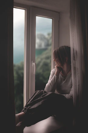 A woman sits by a window, gazing out.