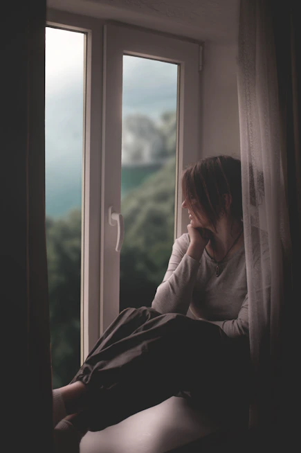 A woman sits by a window, gazing out.