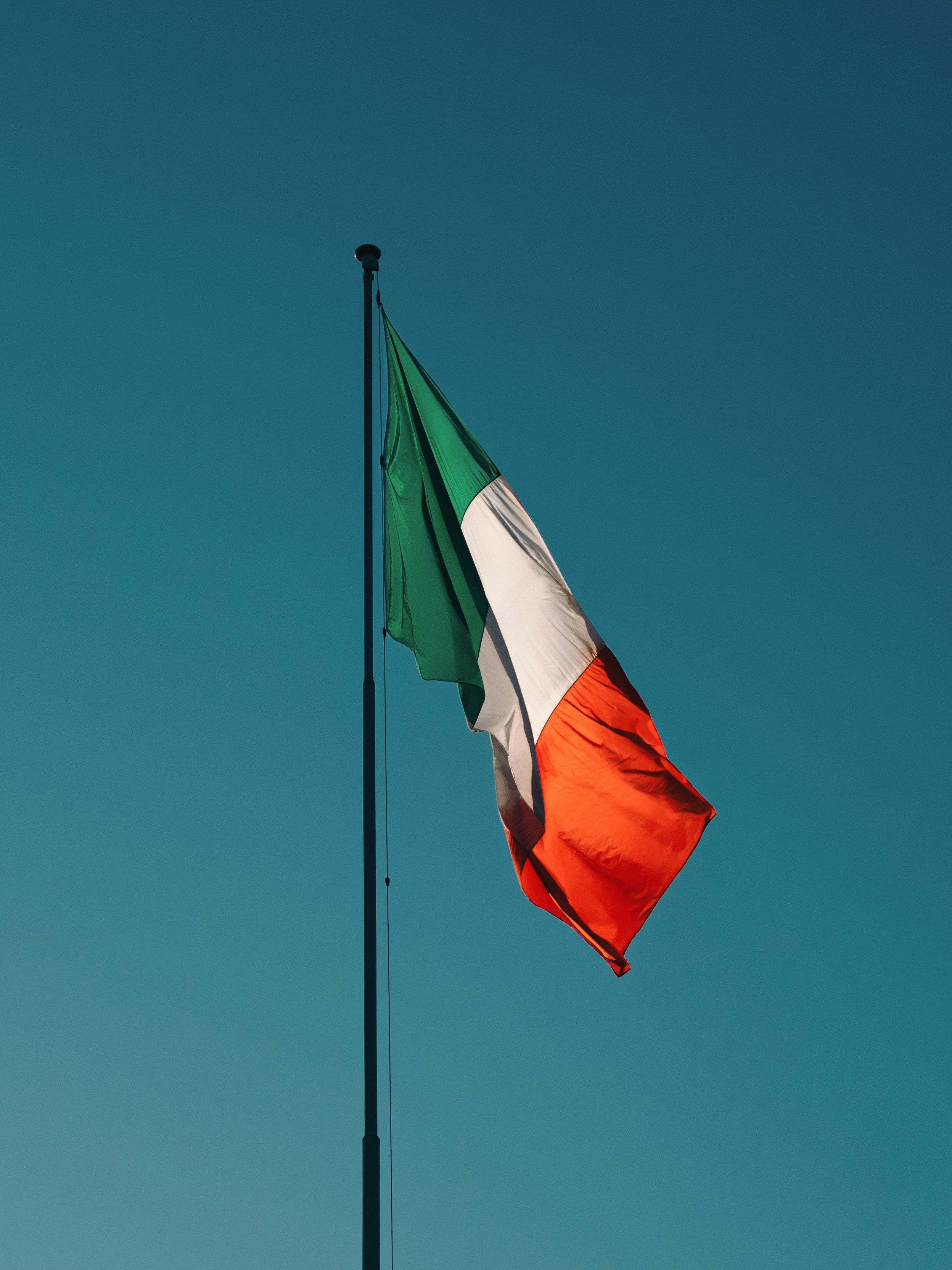 The irish flag is waving in a bright, blue sky.