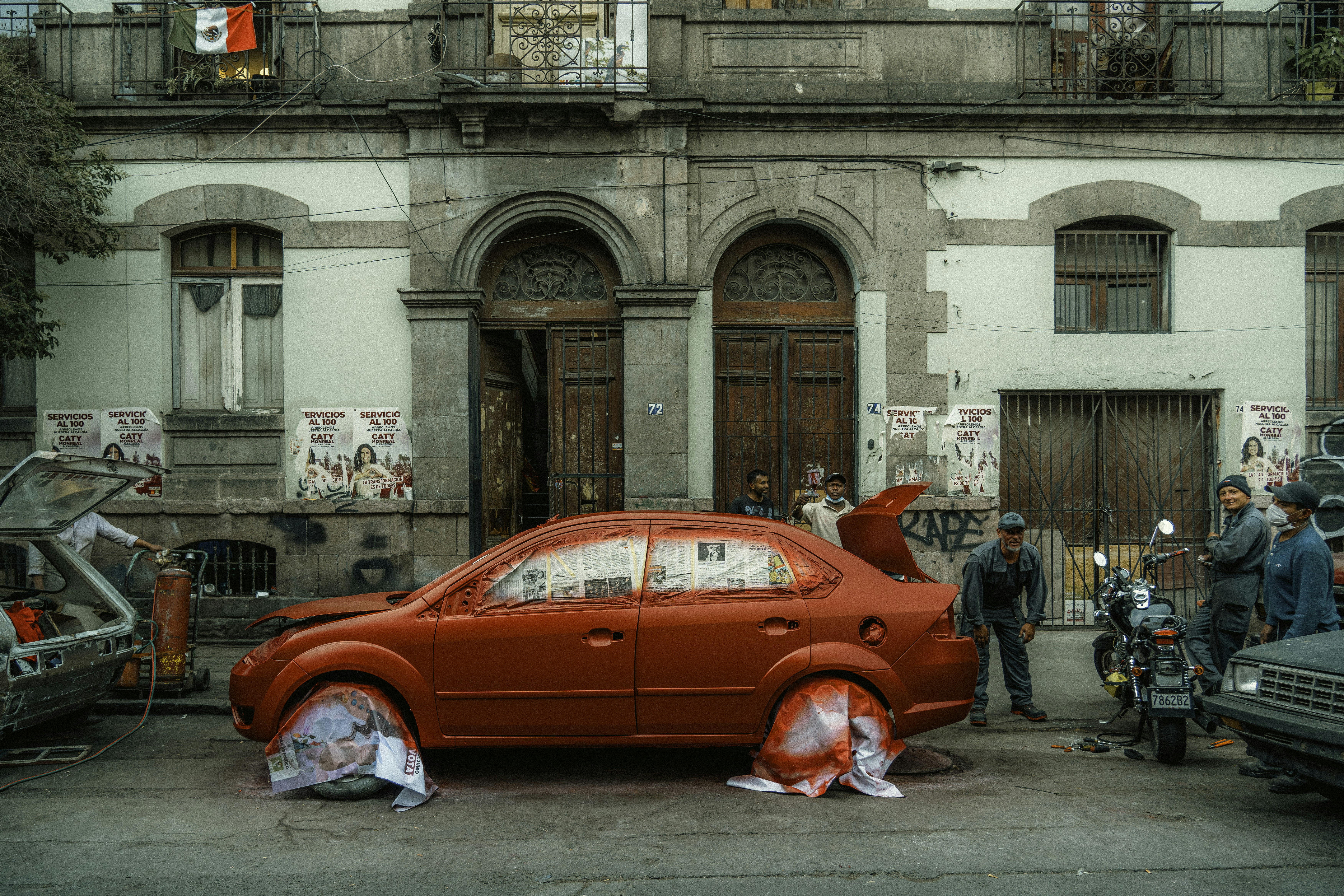 A red car is being painted on a city street.