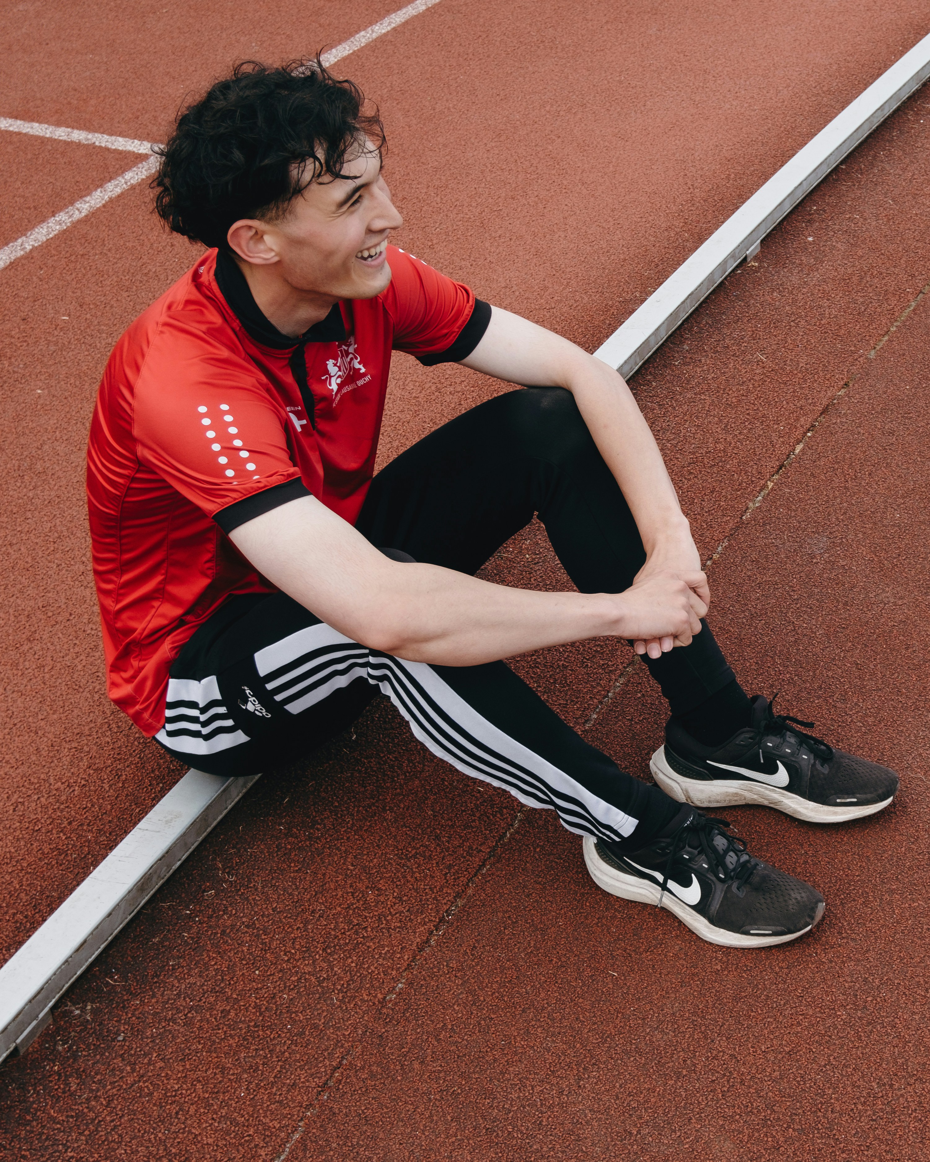 A young man sits on a track, smiling.