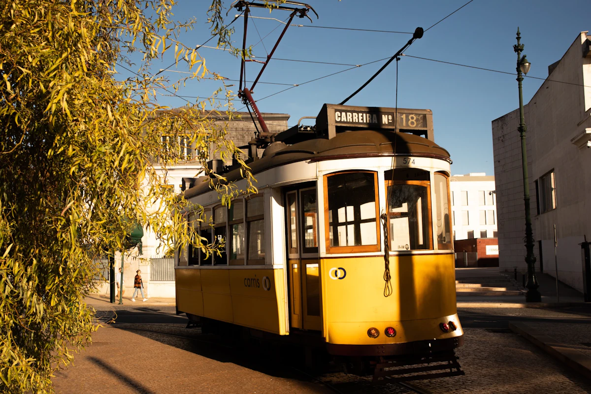 A classic yellow tram travelling down a sunny cobblestone street in Lisbon
