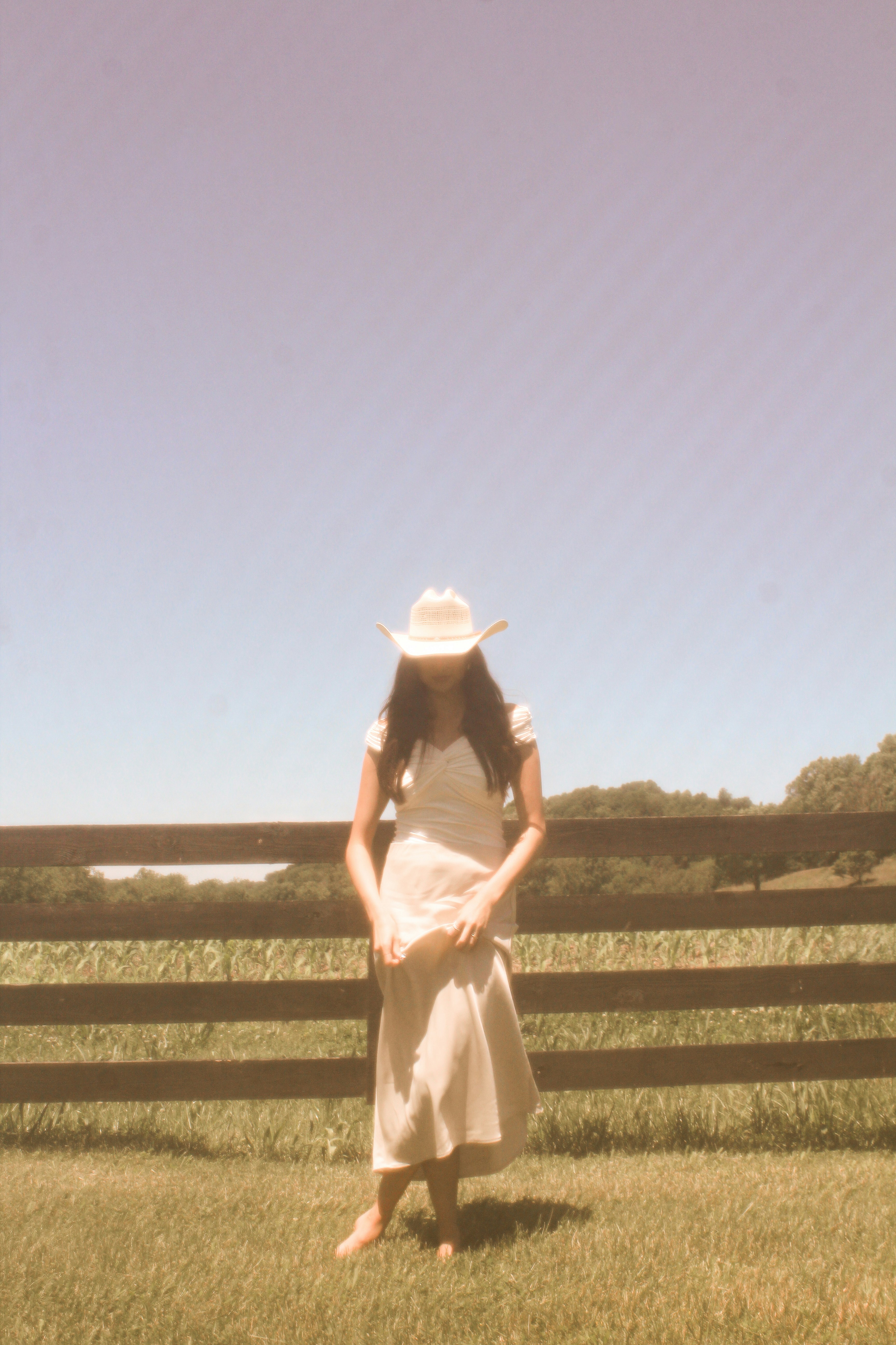Woman in a cowboy hat stands by a fence.