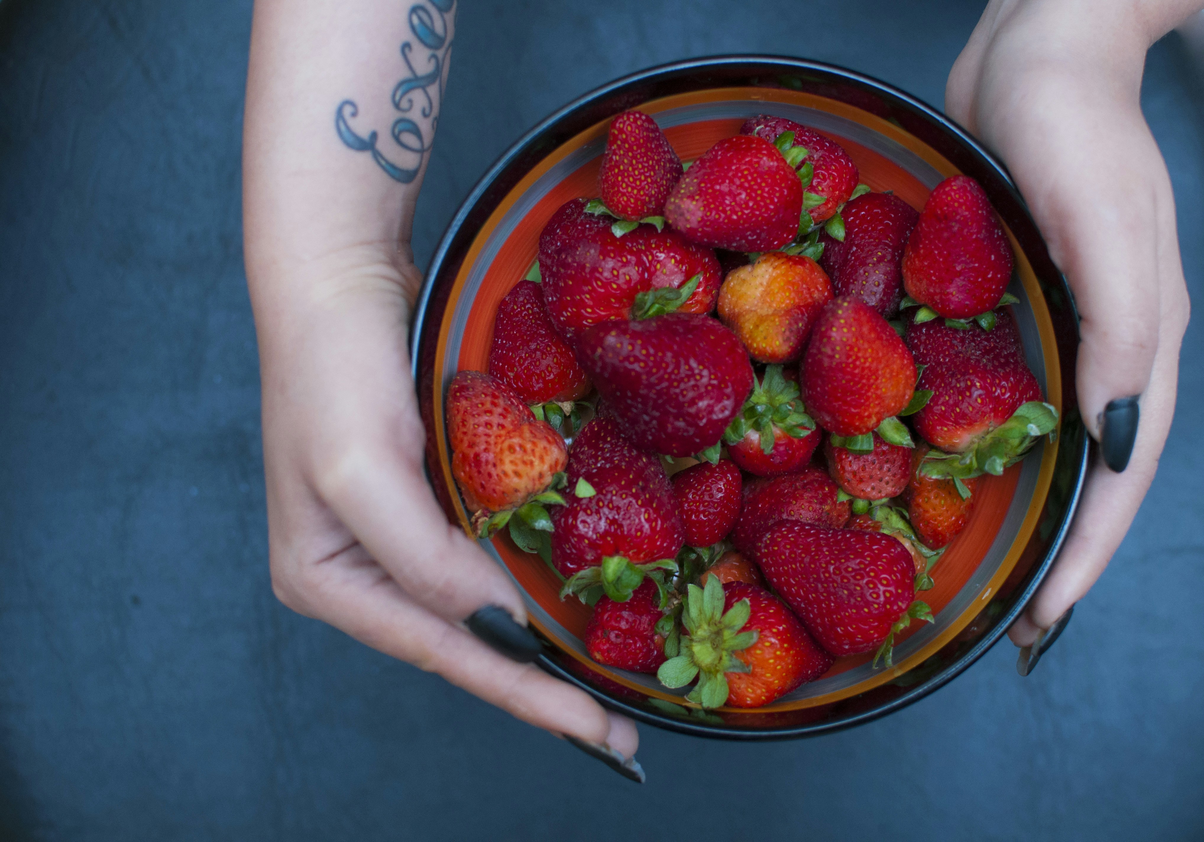 Hands hold a bowl full of fresh strawberries.