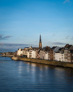 Cityscape with buildings and a river under a blue sky.