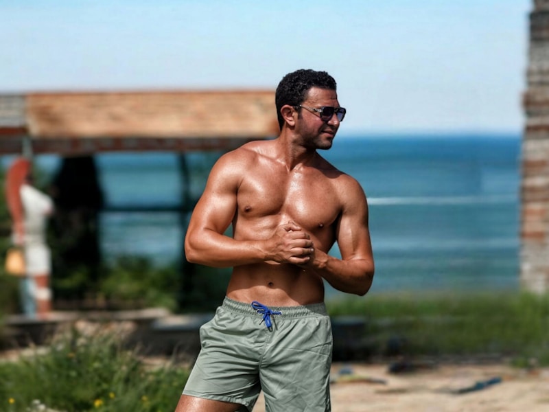 Muscular man poses shirtless by the water.