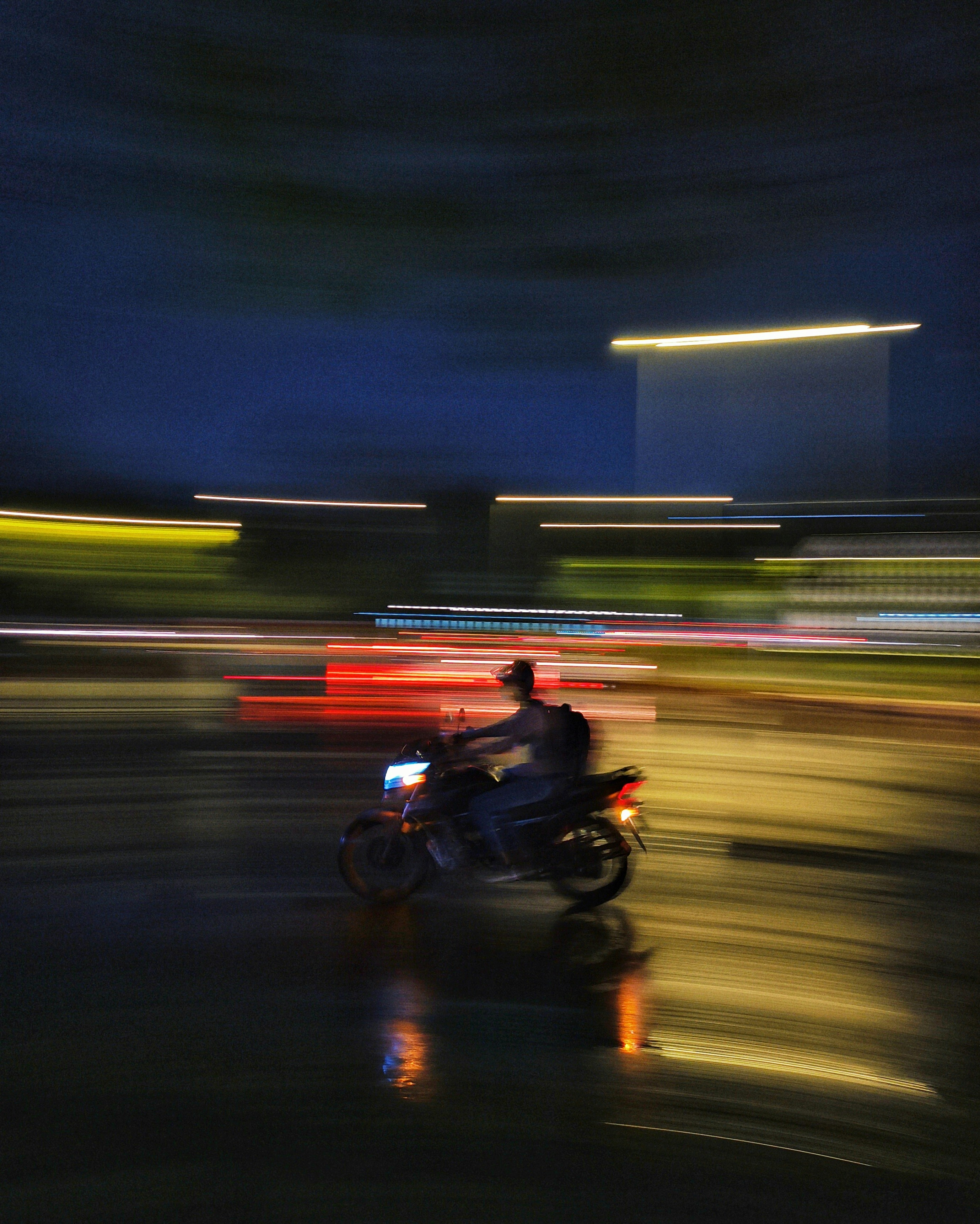 El motociclista acelera a través de una escena nocturna colorida y borrosa.