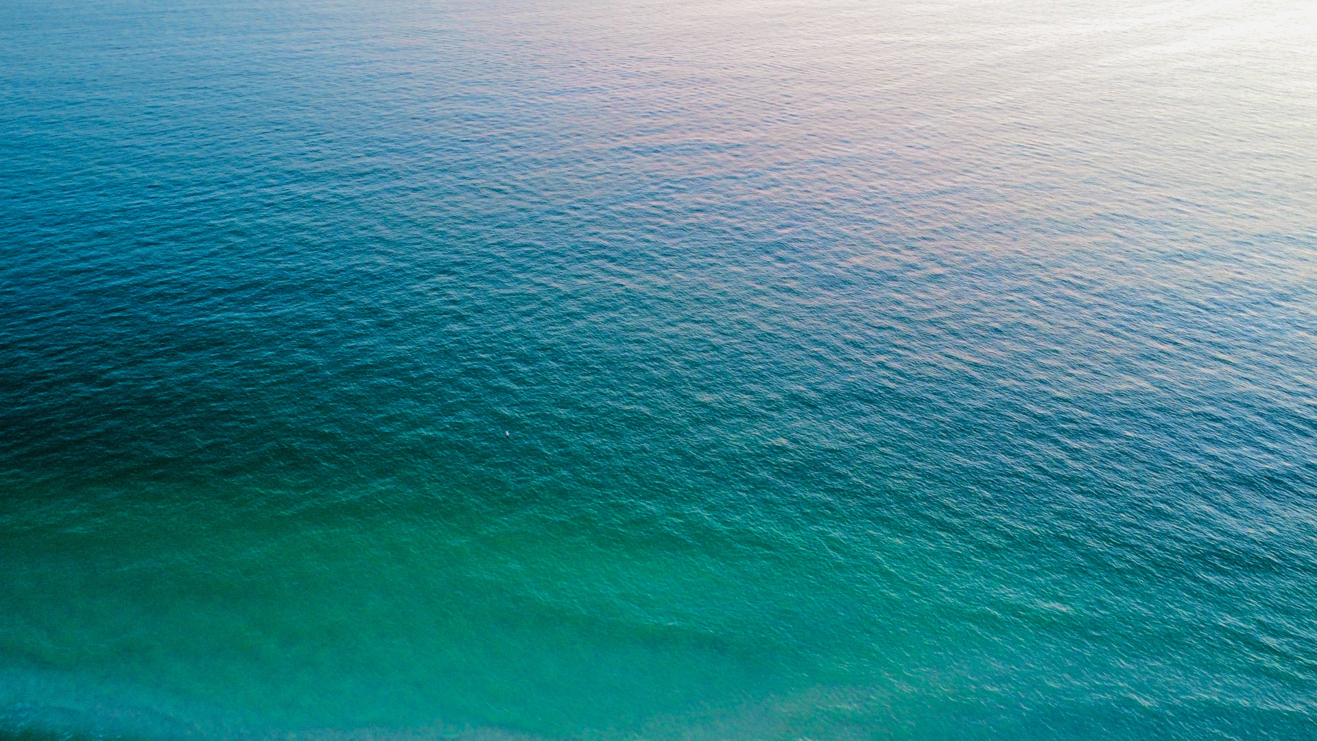 Calm ocean water reflects a bright sky.