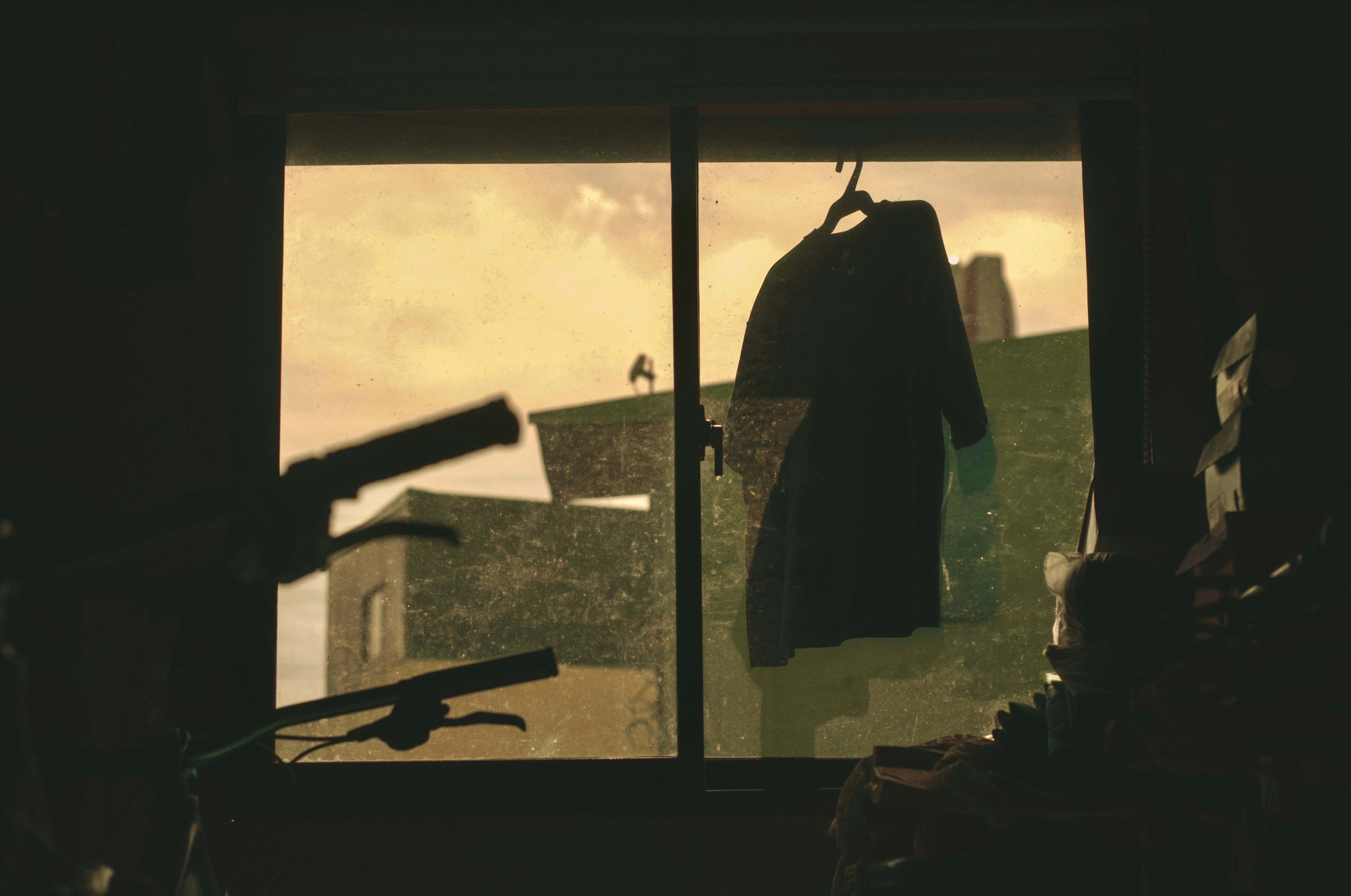 A coat hangs by a window with a cloudy sky.