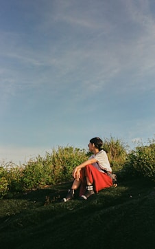A person sits in the grass, looking away.