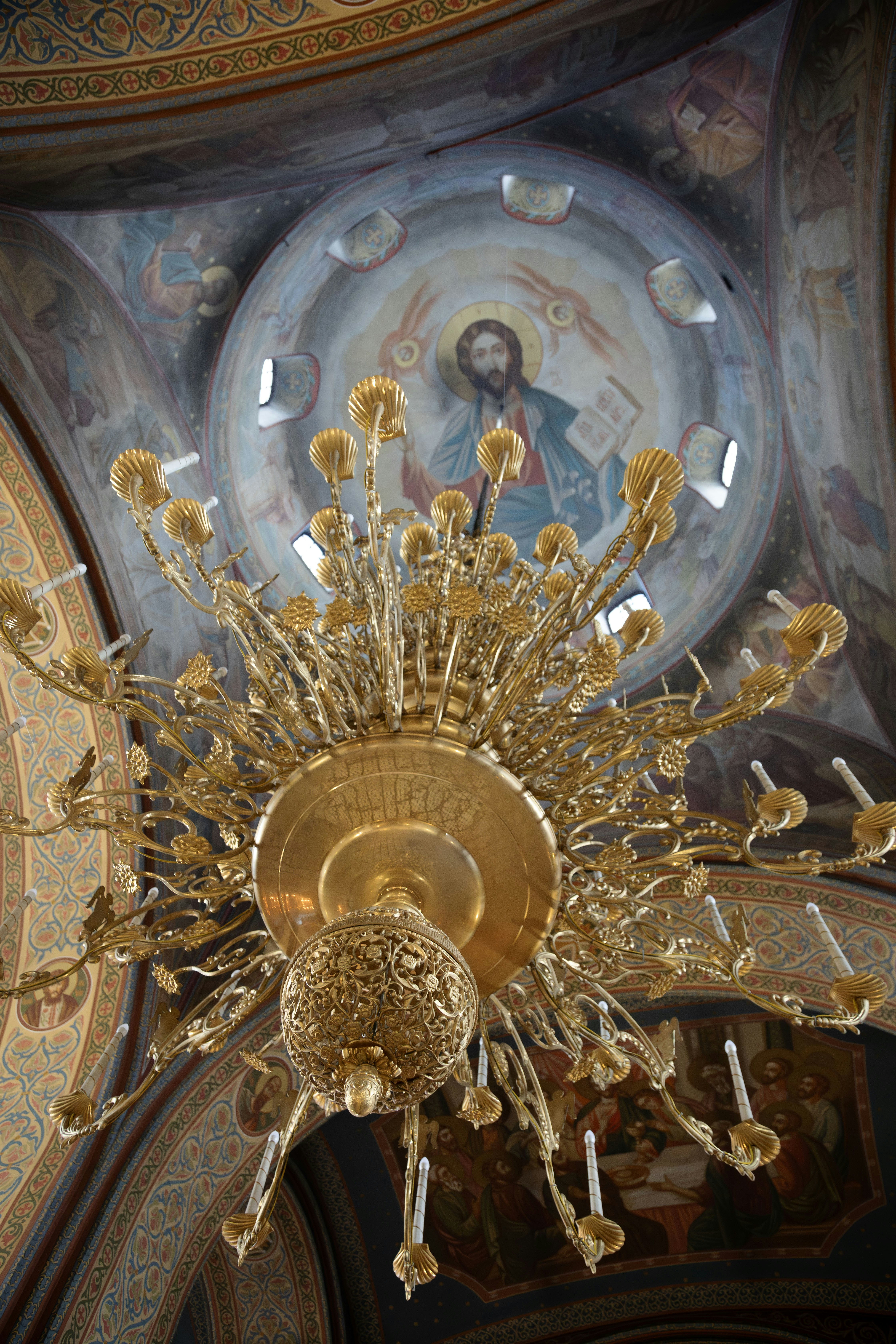 A golden chandelier hangs below a painted ceiling.