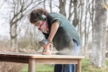 A woman is sanding a wooden table outdoors.