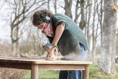 A woman is sanding a wooden table outdoors.