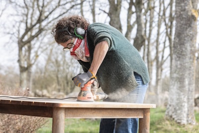 A woman is sanding a wooden table outdoors.
