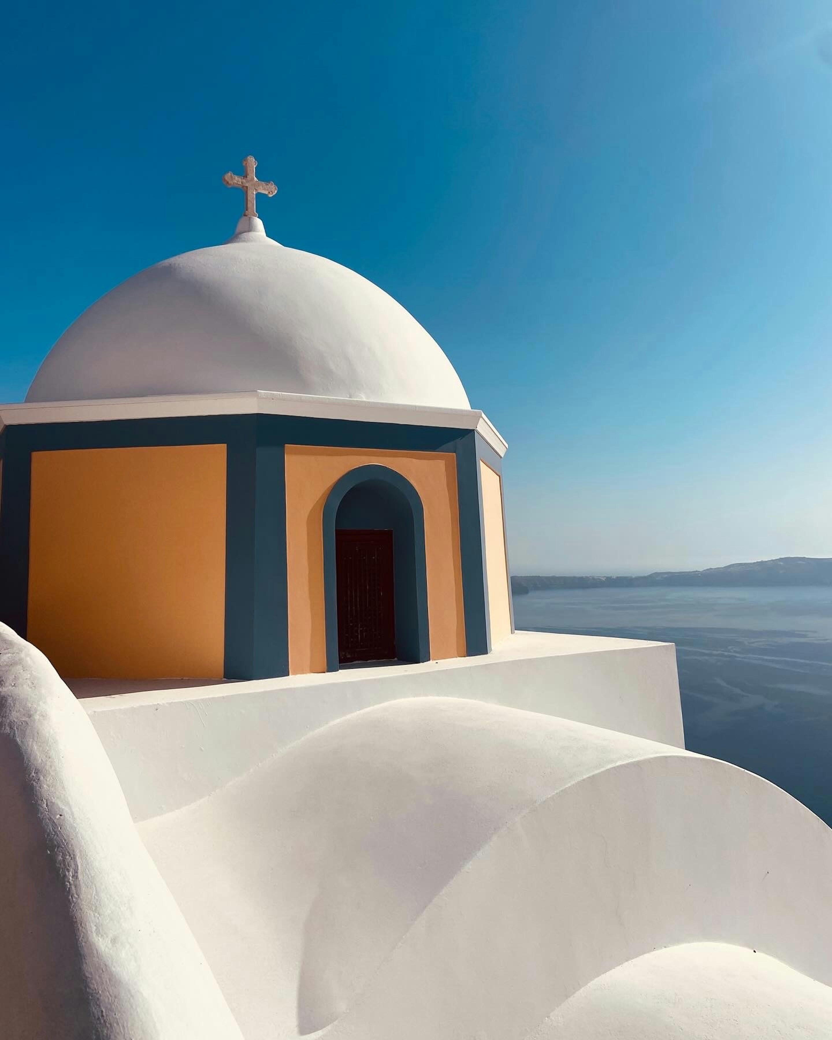 A white church stands in greece with the sea.