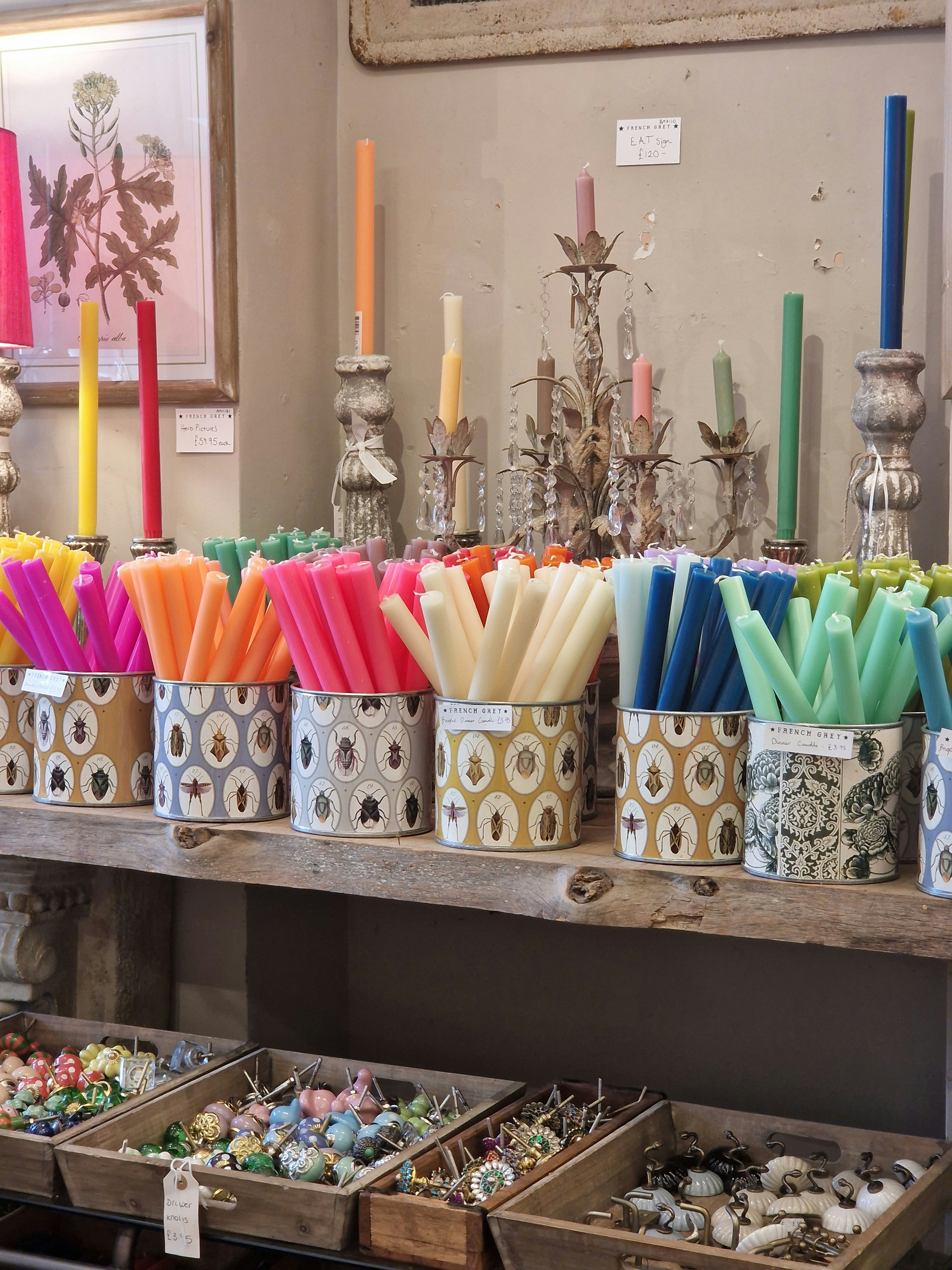 Des bougies colorées sont exposées sur une étagère en bois.