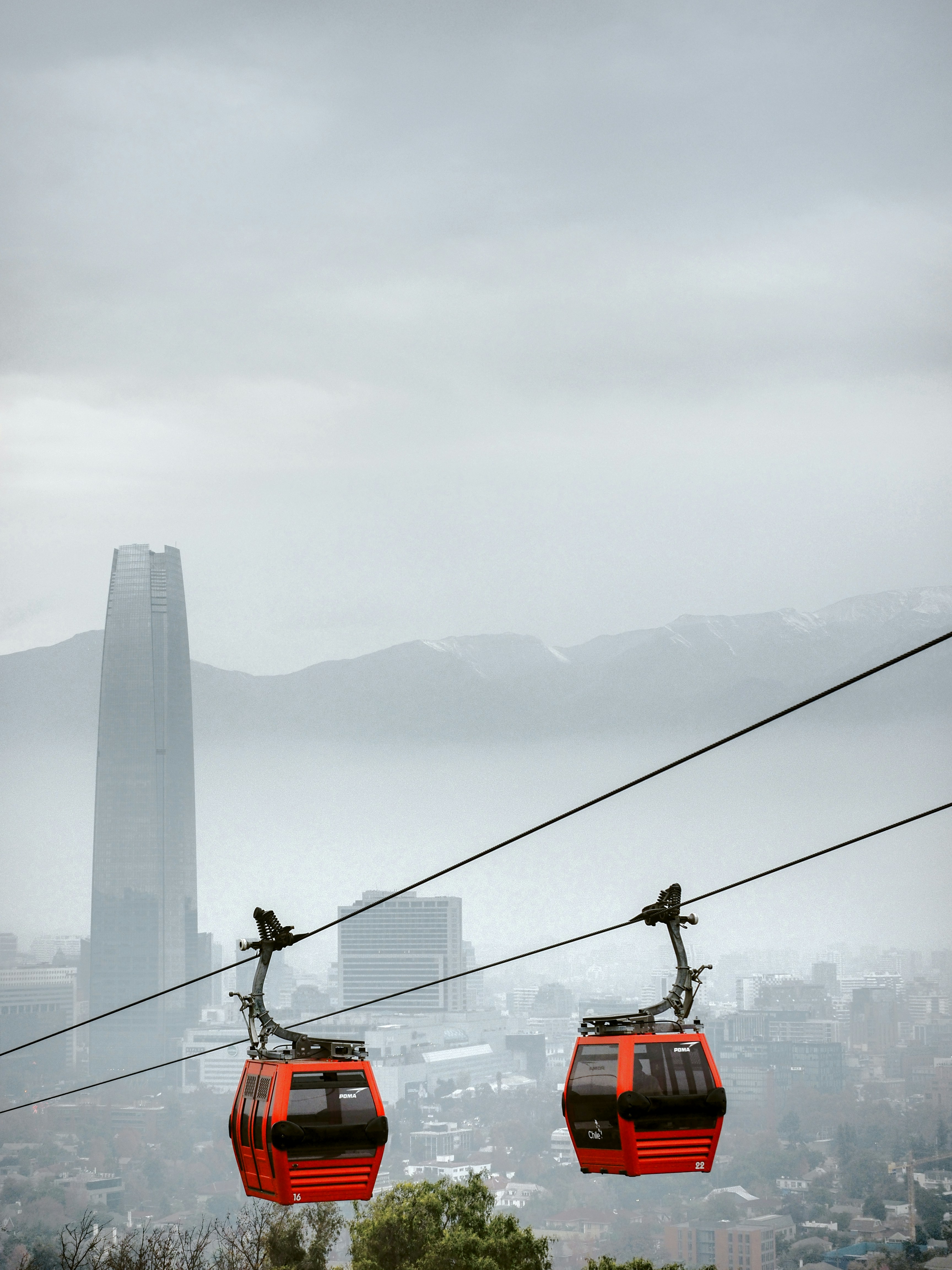 Cable cars travel above a city on a cloudy day.