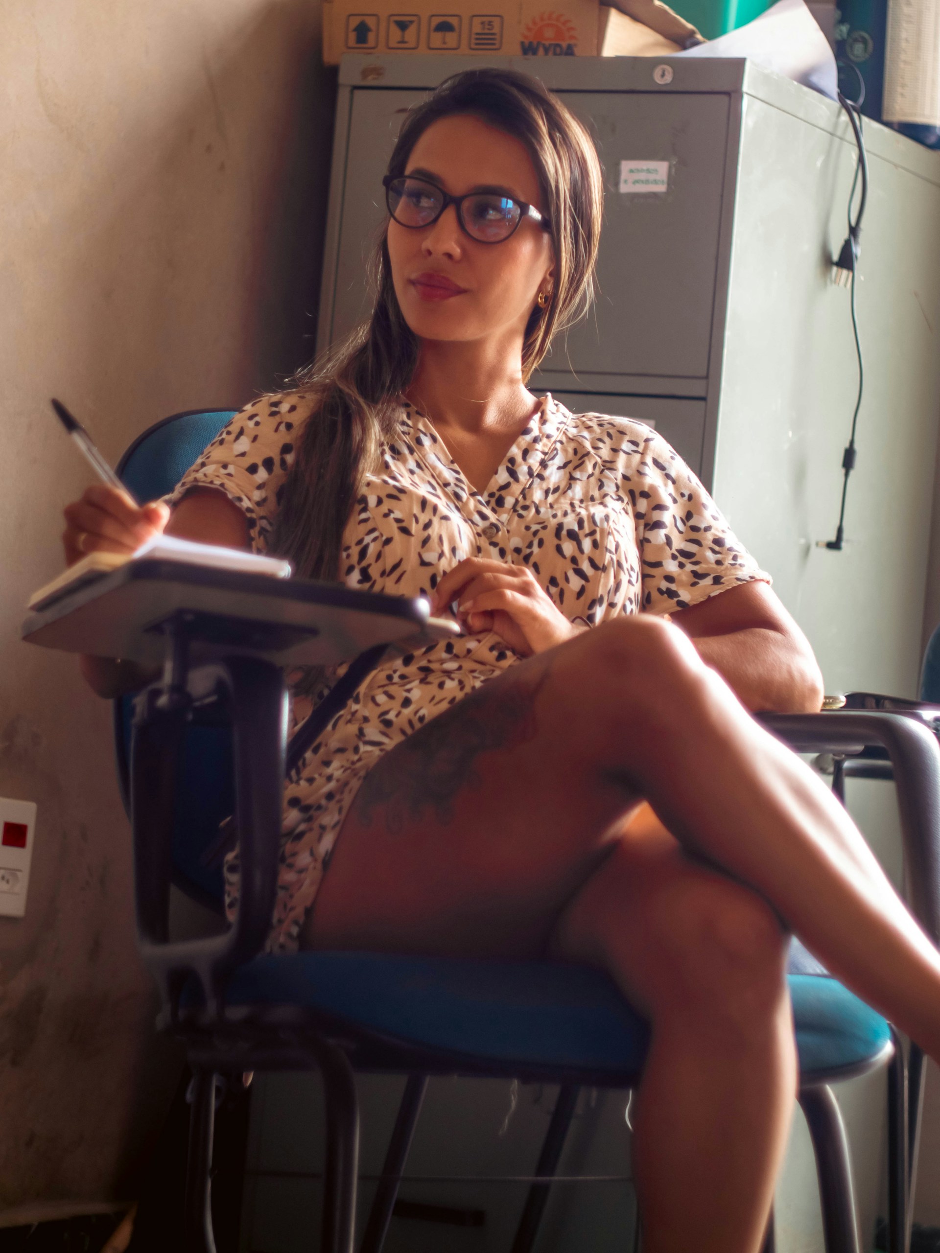 A woman with glasses is writing at her desk.