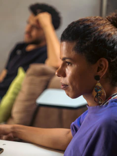 Woman looks ahead with a person in the background.