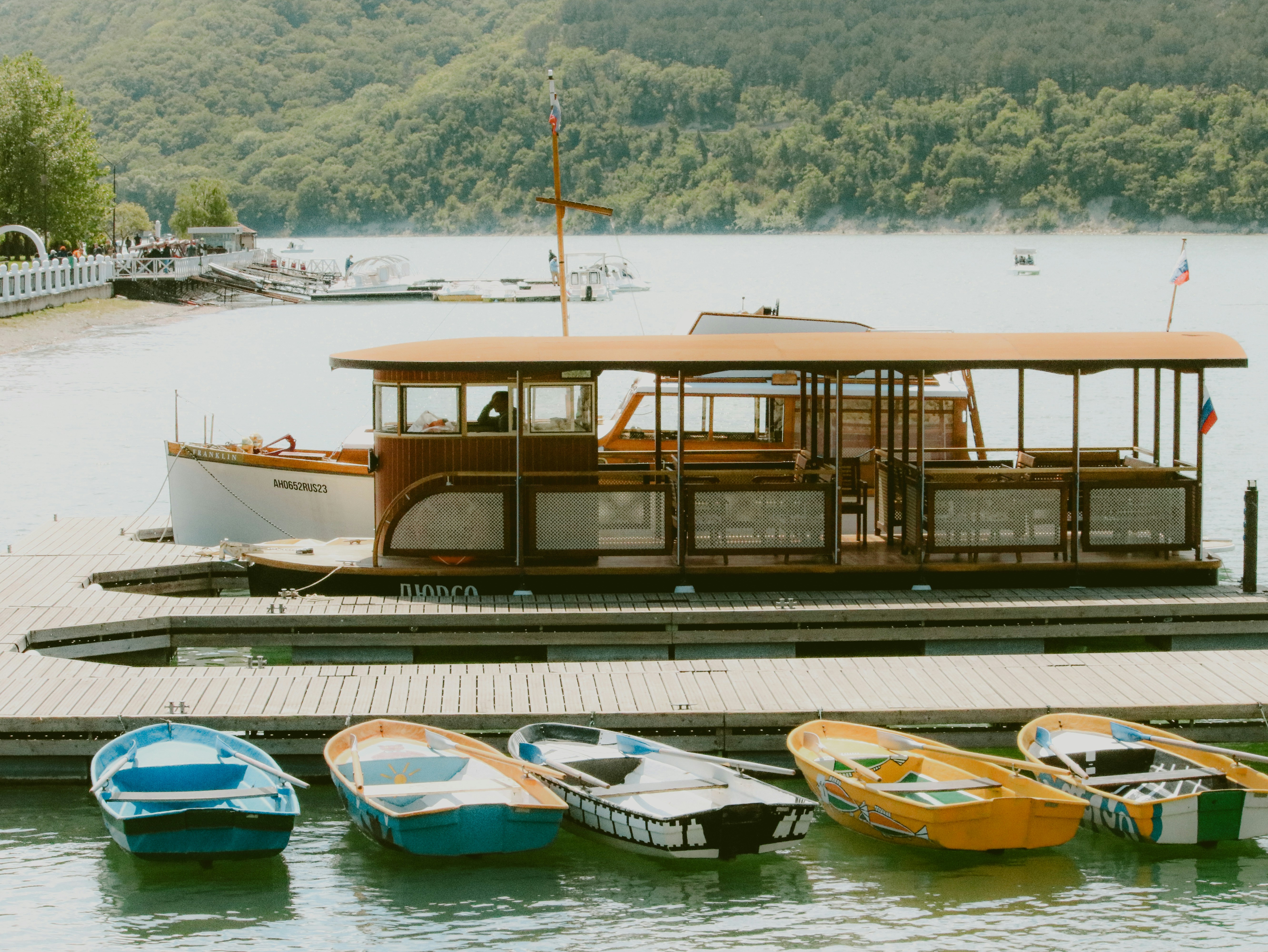 A wooden boat docks near smaller boats.