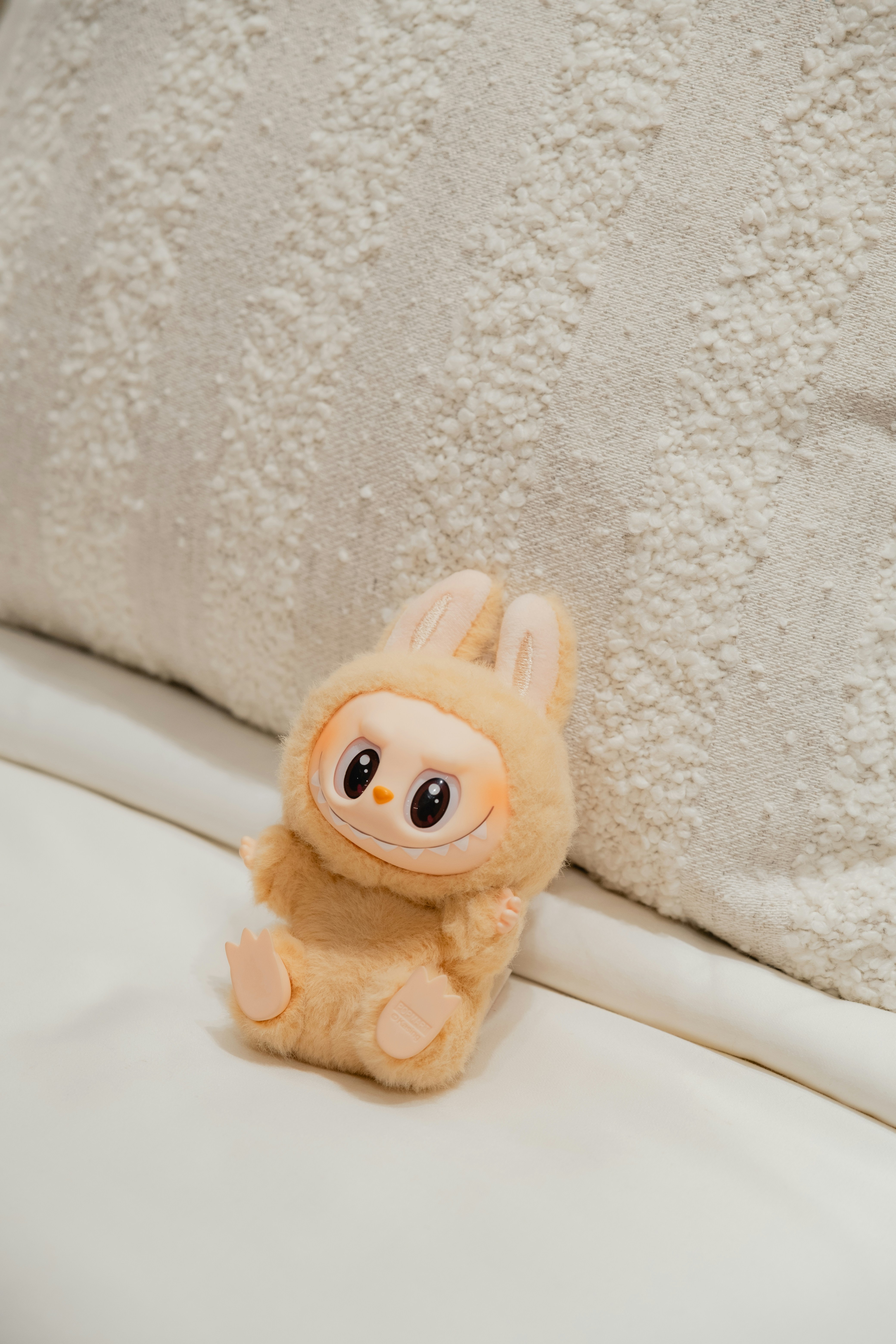 A cute bunny plush toy sits on a bed.