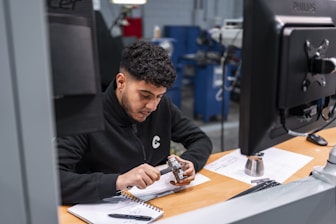 A man measures a metal component carefully.