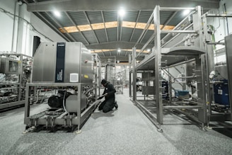 A worker repairs machinery in a factory setting.
