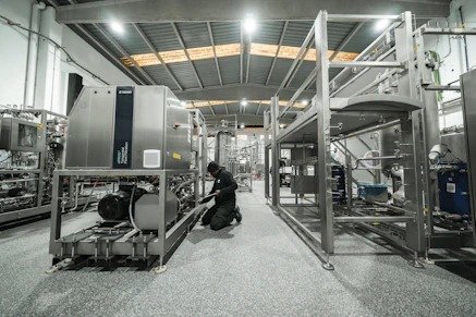 A worker repairs machinery in a factory setting.