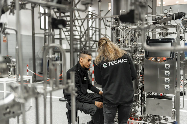 Two people work on complex industrial equipment.