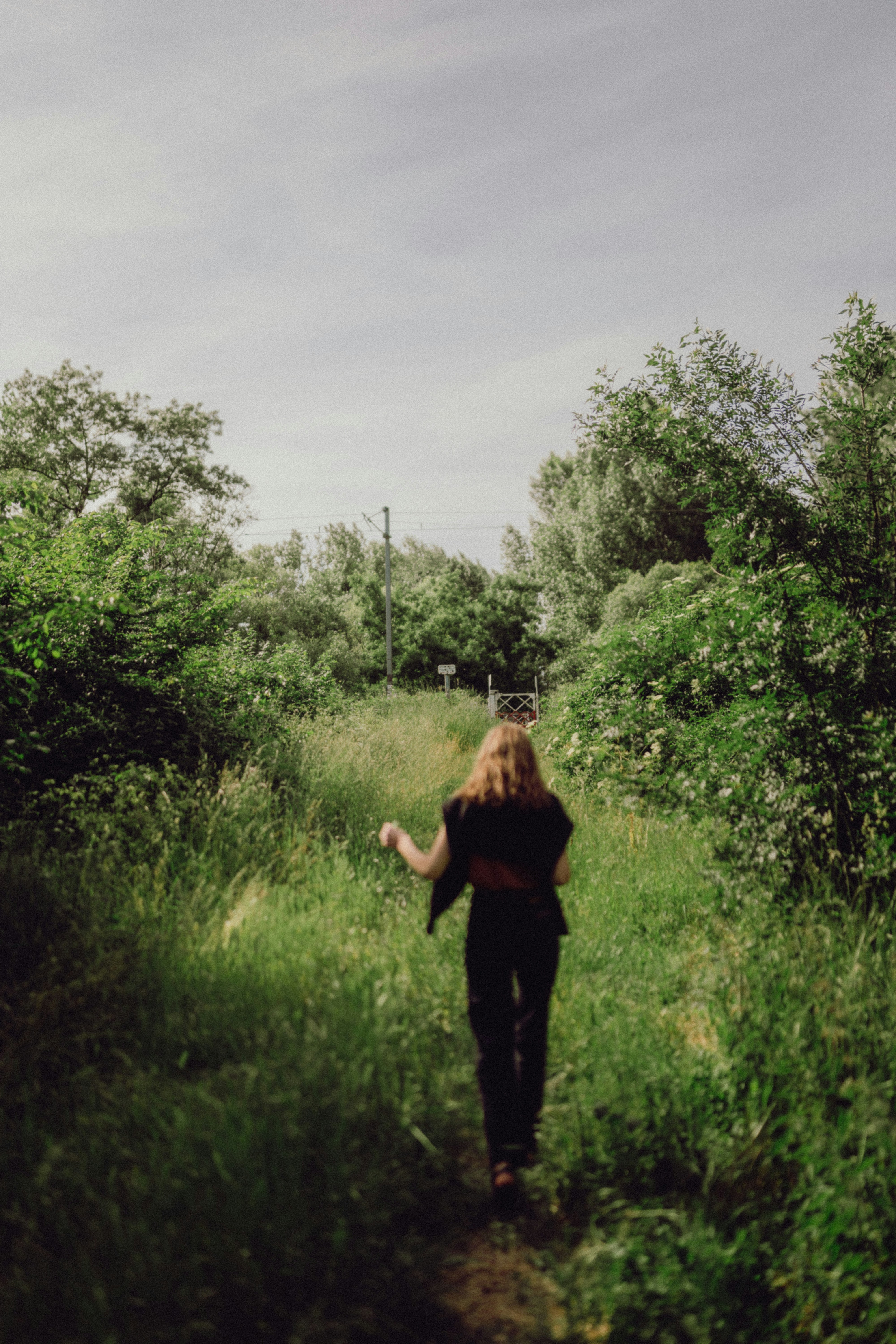 Woman walks through a grassy path in nature.
