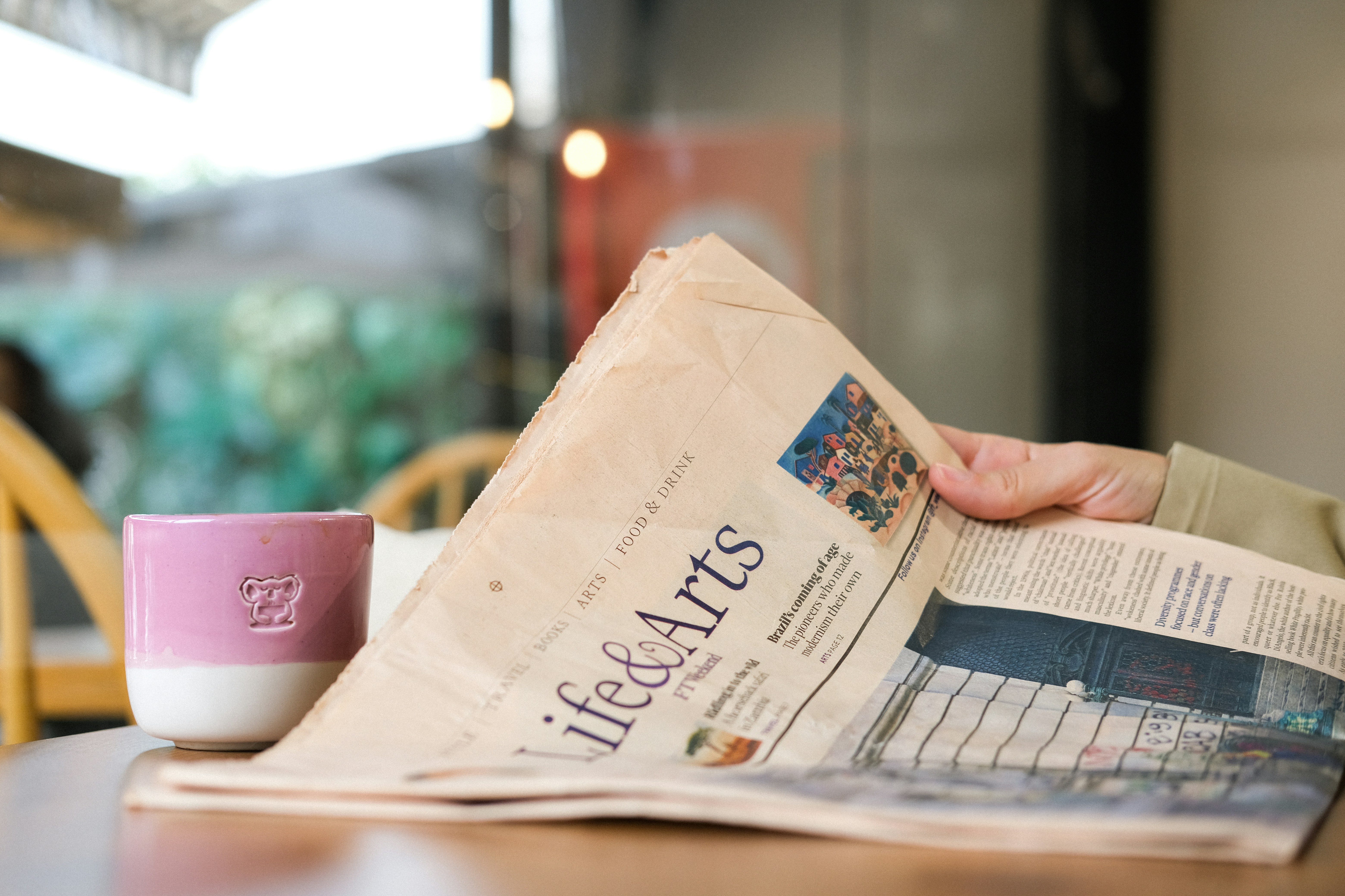 Seseorang sedang membaca koran dengan kopi.