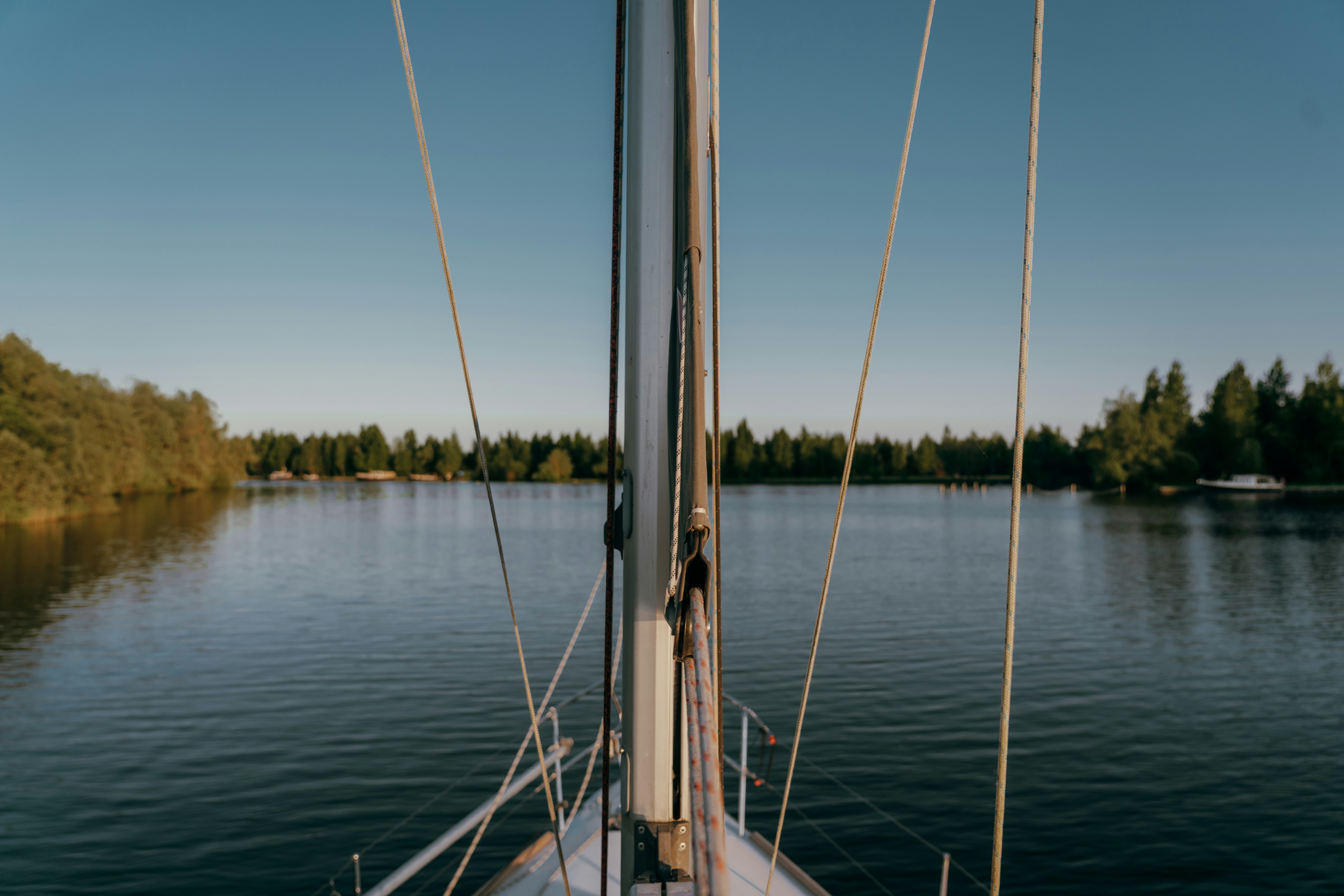 Sailboat sails on serene water toward trees.
