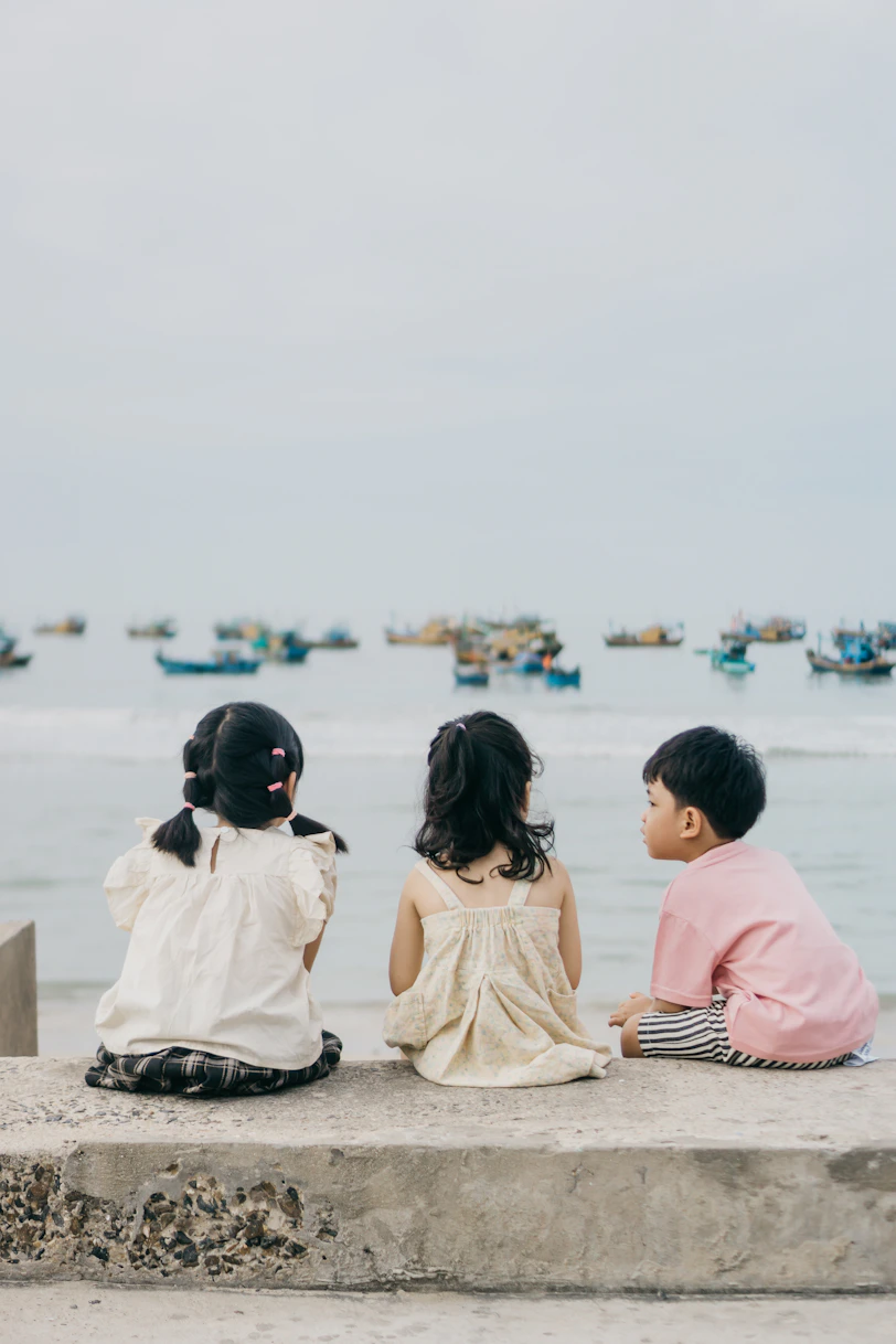 Three children sit and gaze at the sea