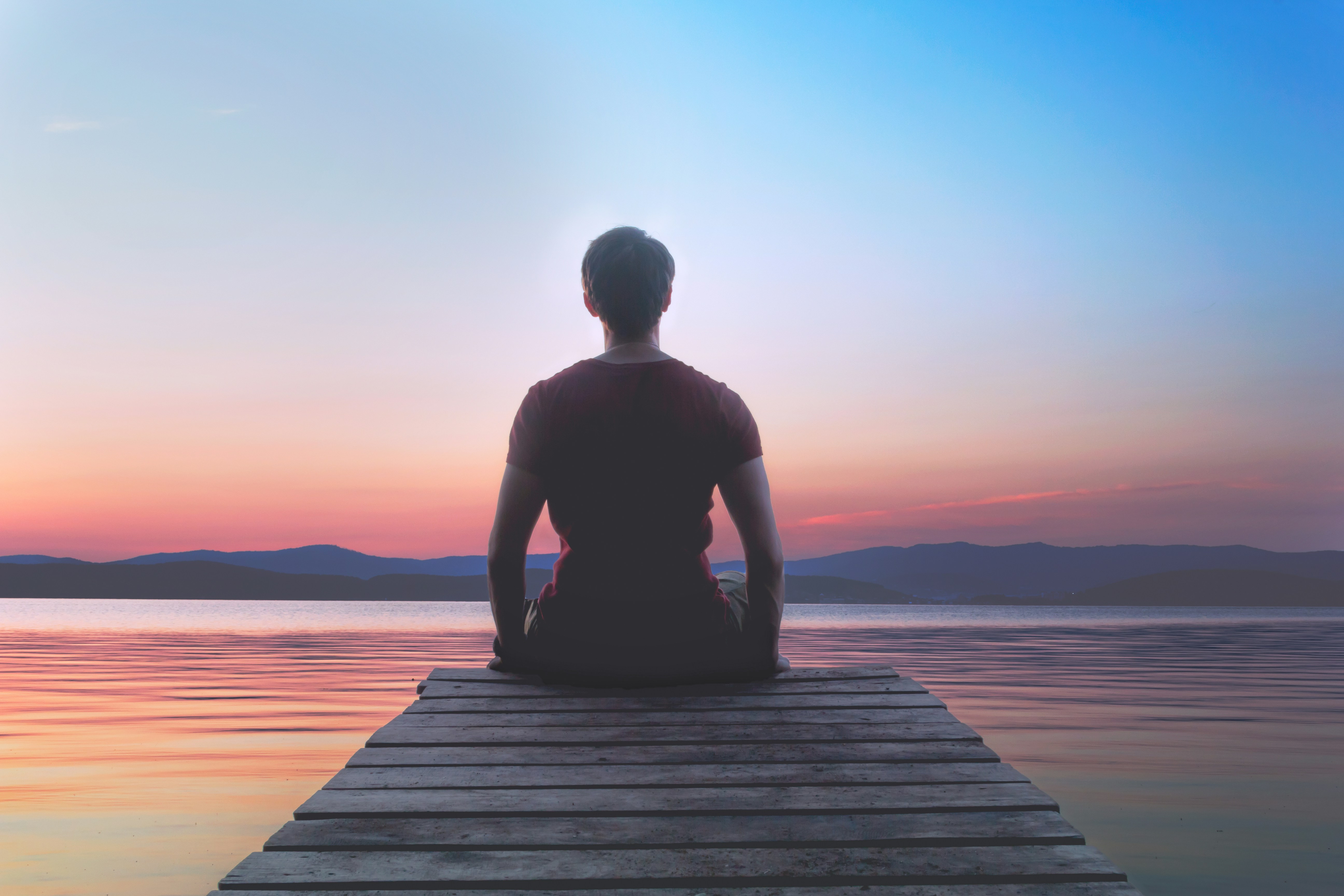 Man meditates on dock watching the sunset