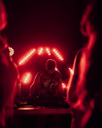 A dj performs in front of a red light display.
