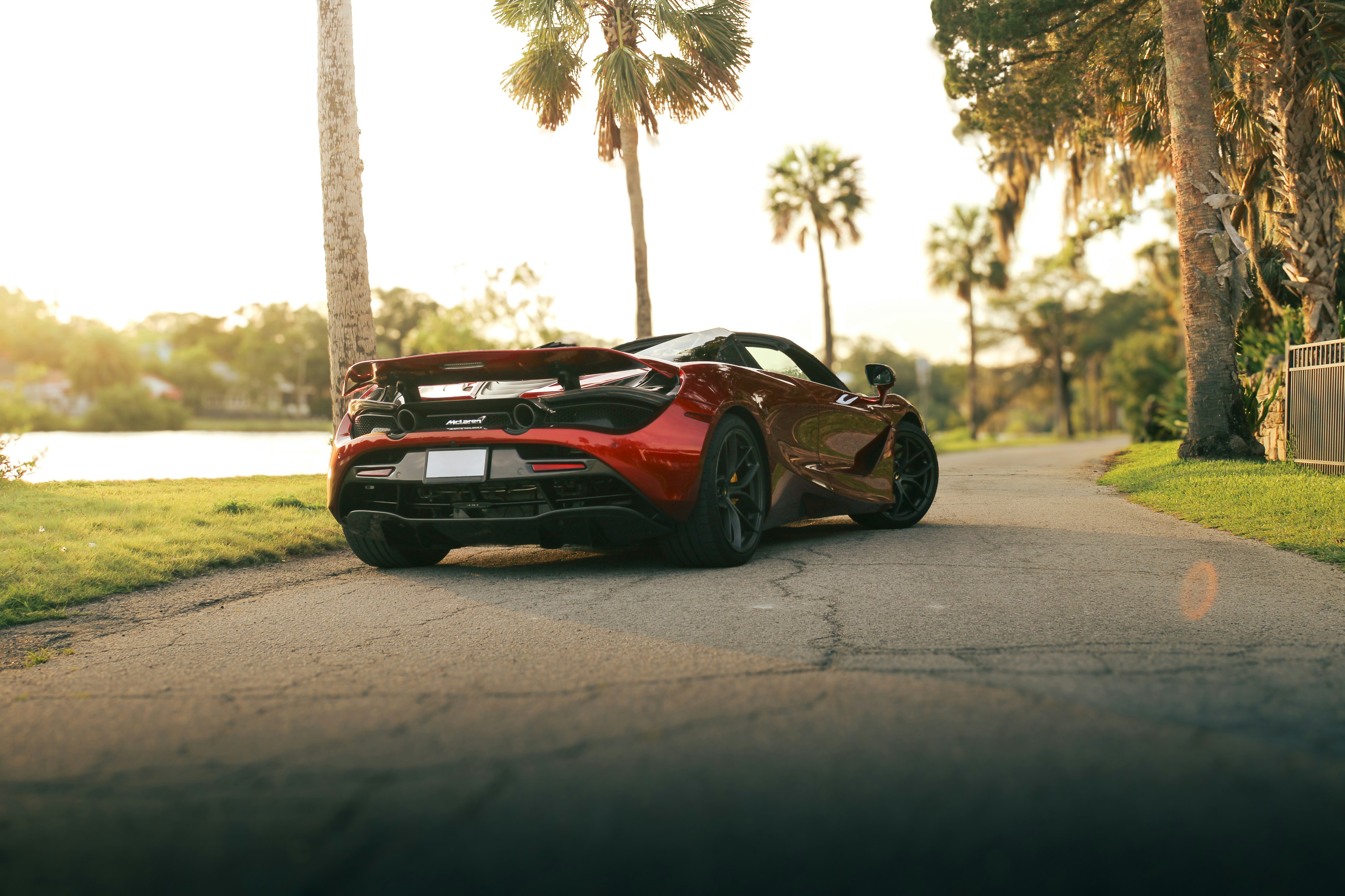 A red mclaren cruises down a scenic road.